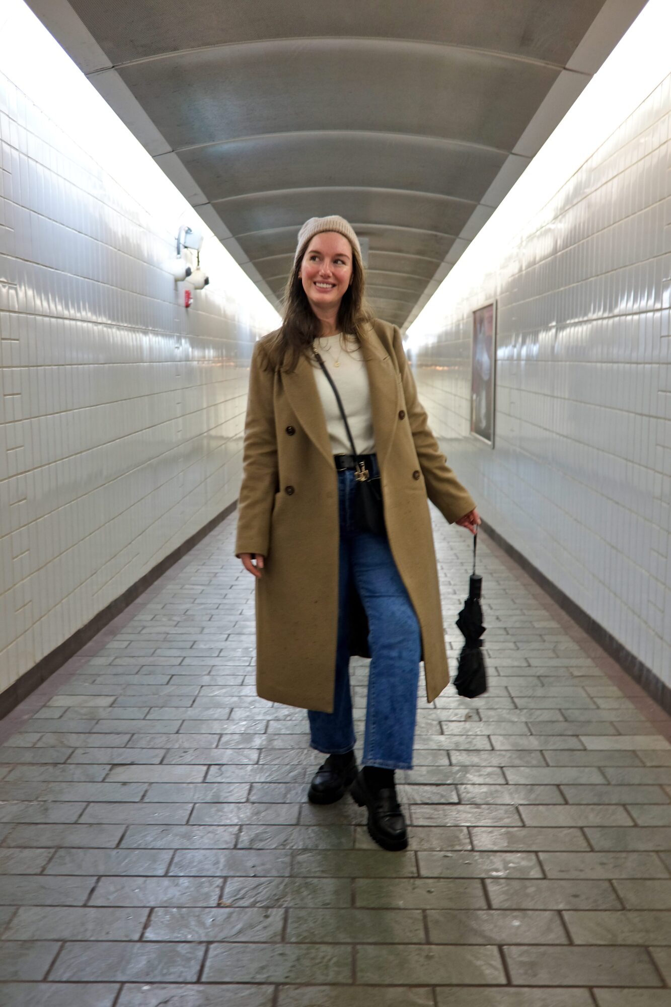 Alyssa wears a white sweater, blue jeans, beanie, and loafers in a T station in Boston