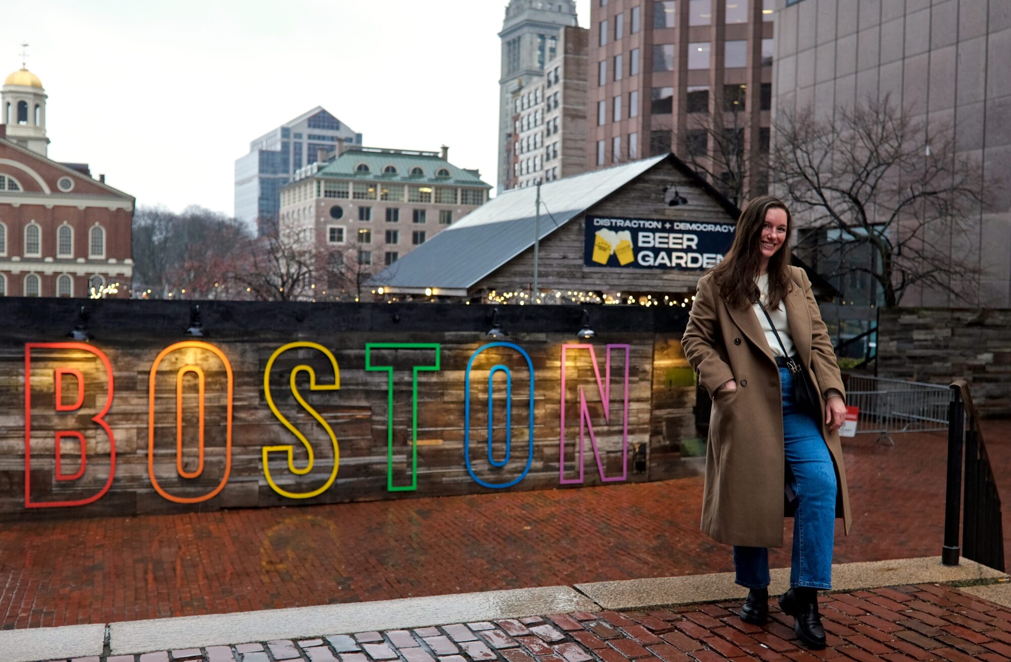 Alyssa wears a white sweater with blue jeans and a camel coat