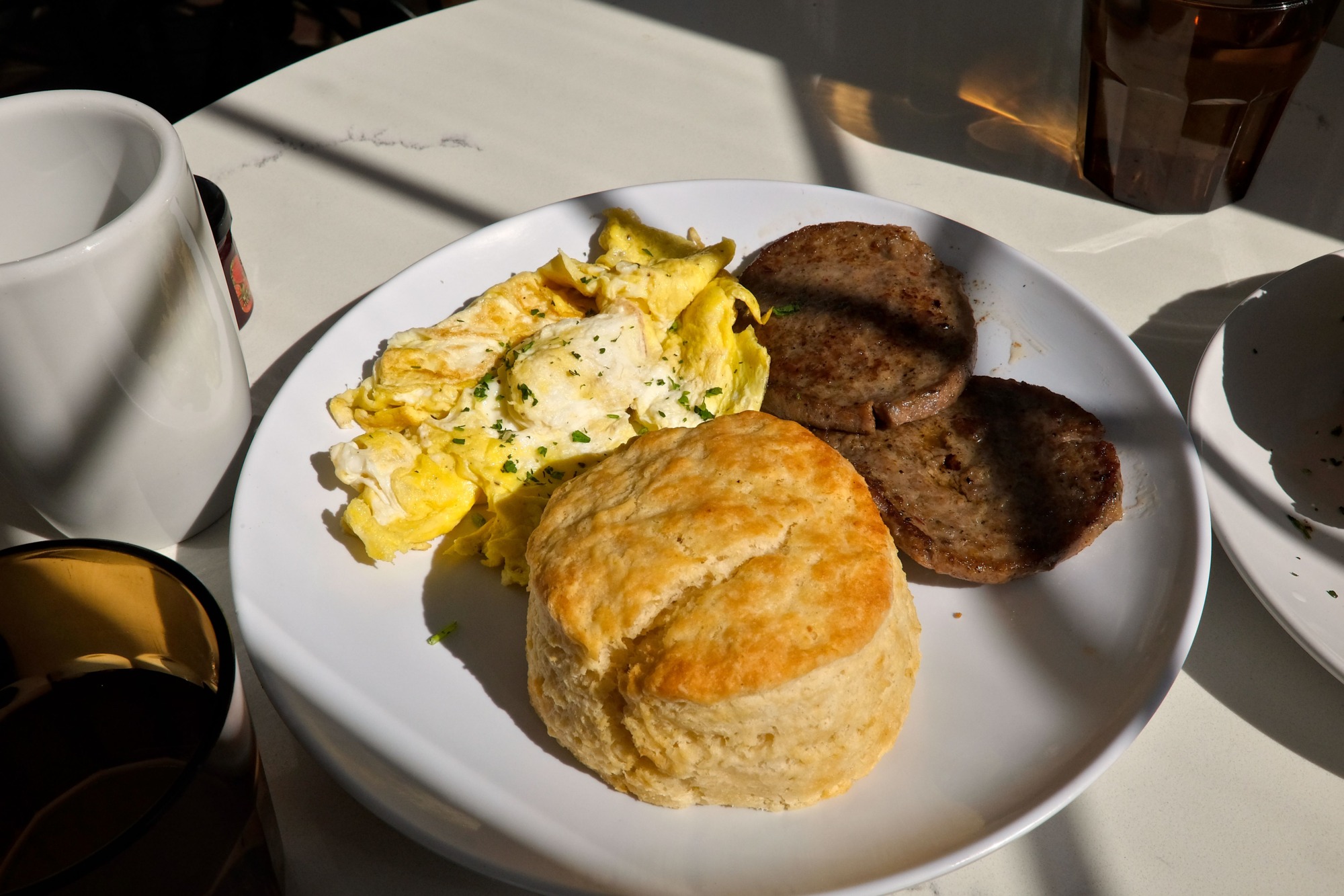 Eggs, sausage, and a biscuit on a light-filled table
