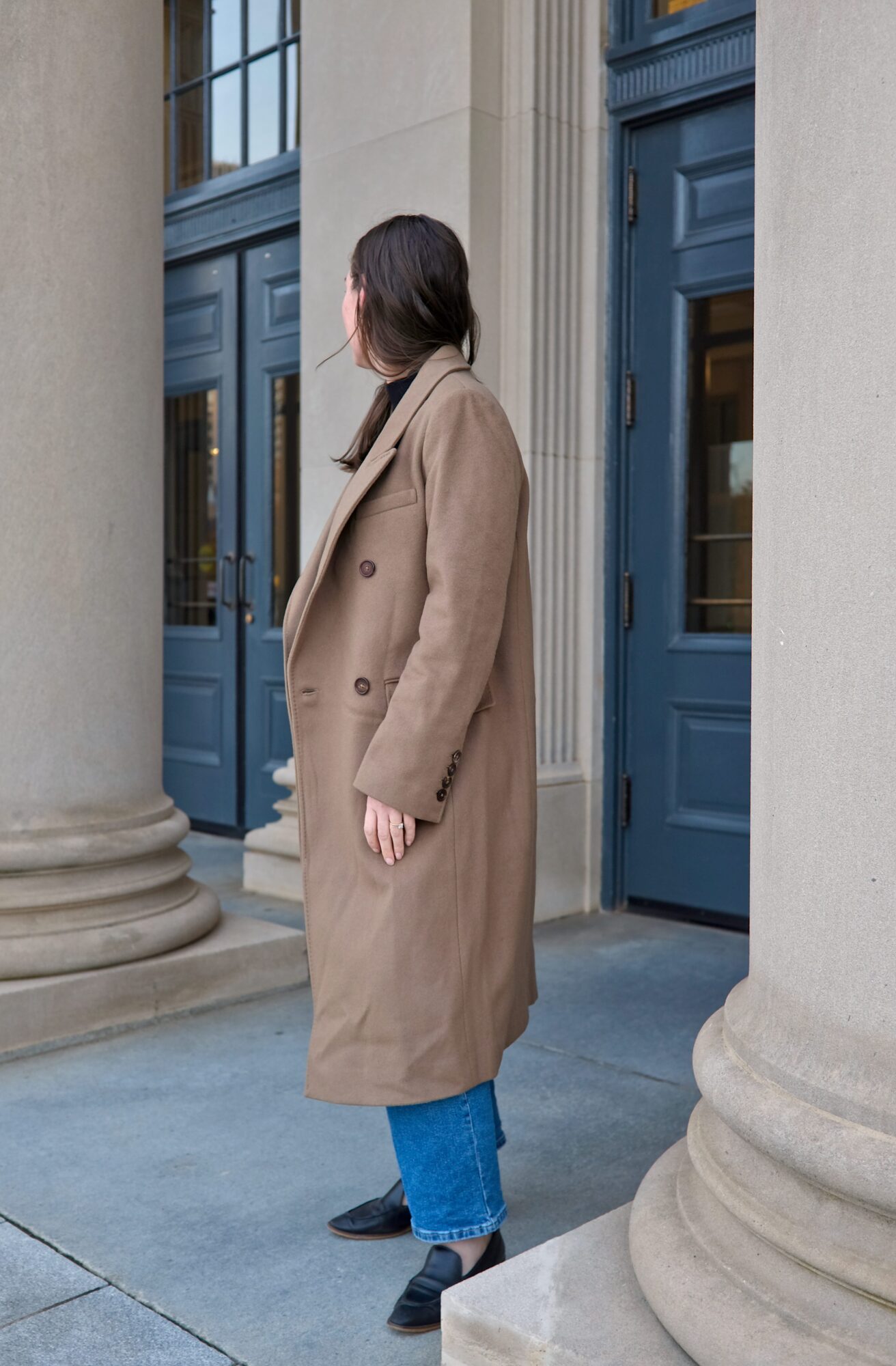 Alyssa wears the Italian Wool Double-Breasted Coat with jeans and a black top and is turned sideways to the camera