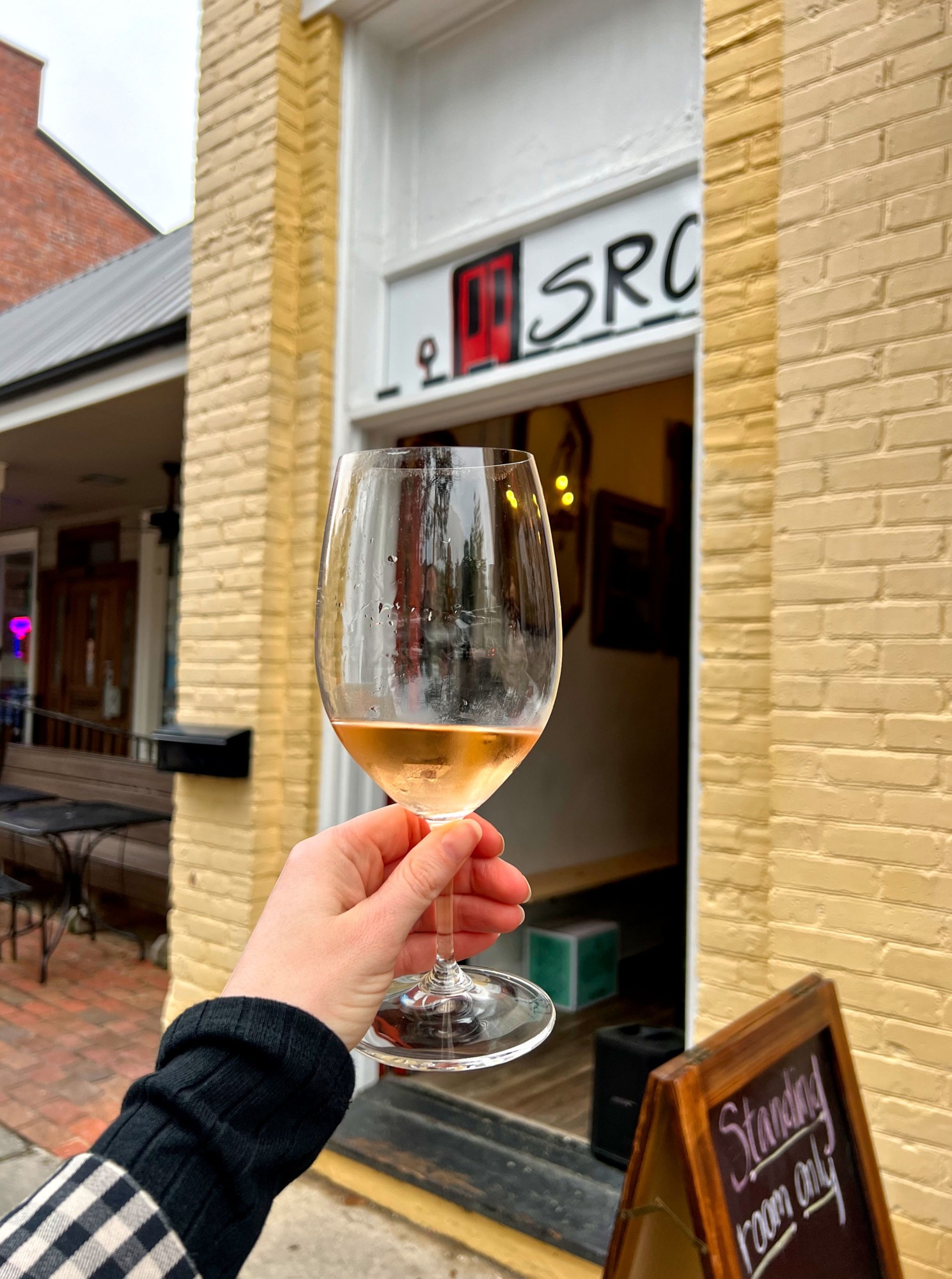 Alyssa holds a glass of wine in front of Standing Room Only