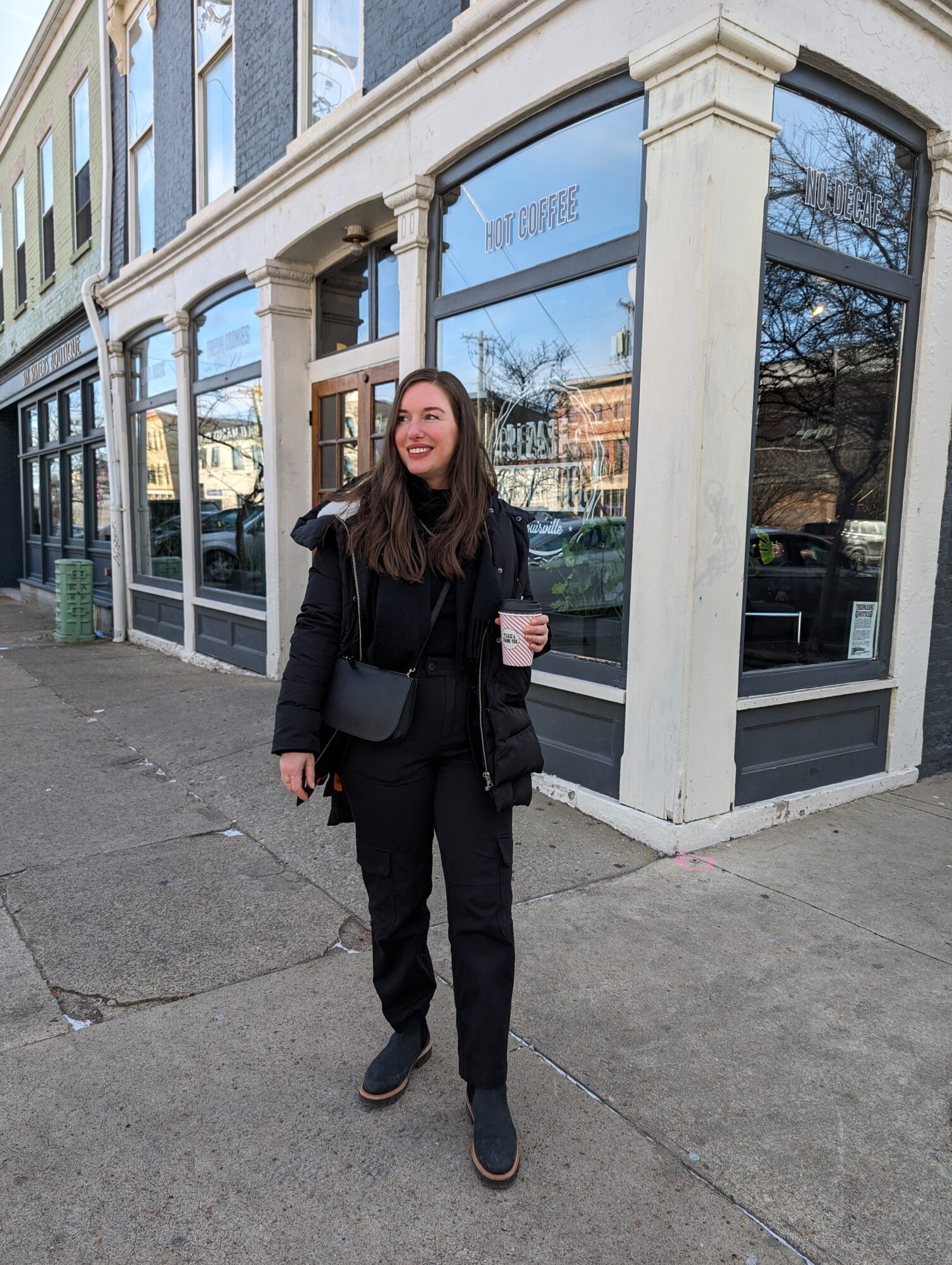 Alyssa carries a cup of coffee in an all-black outfit