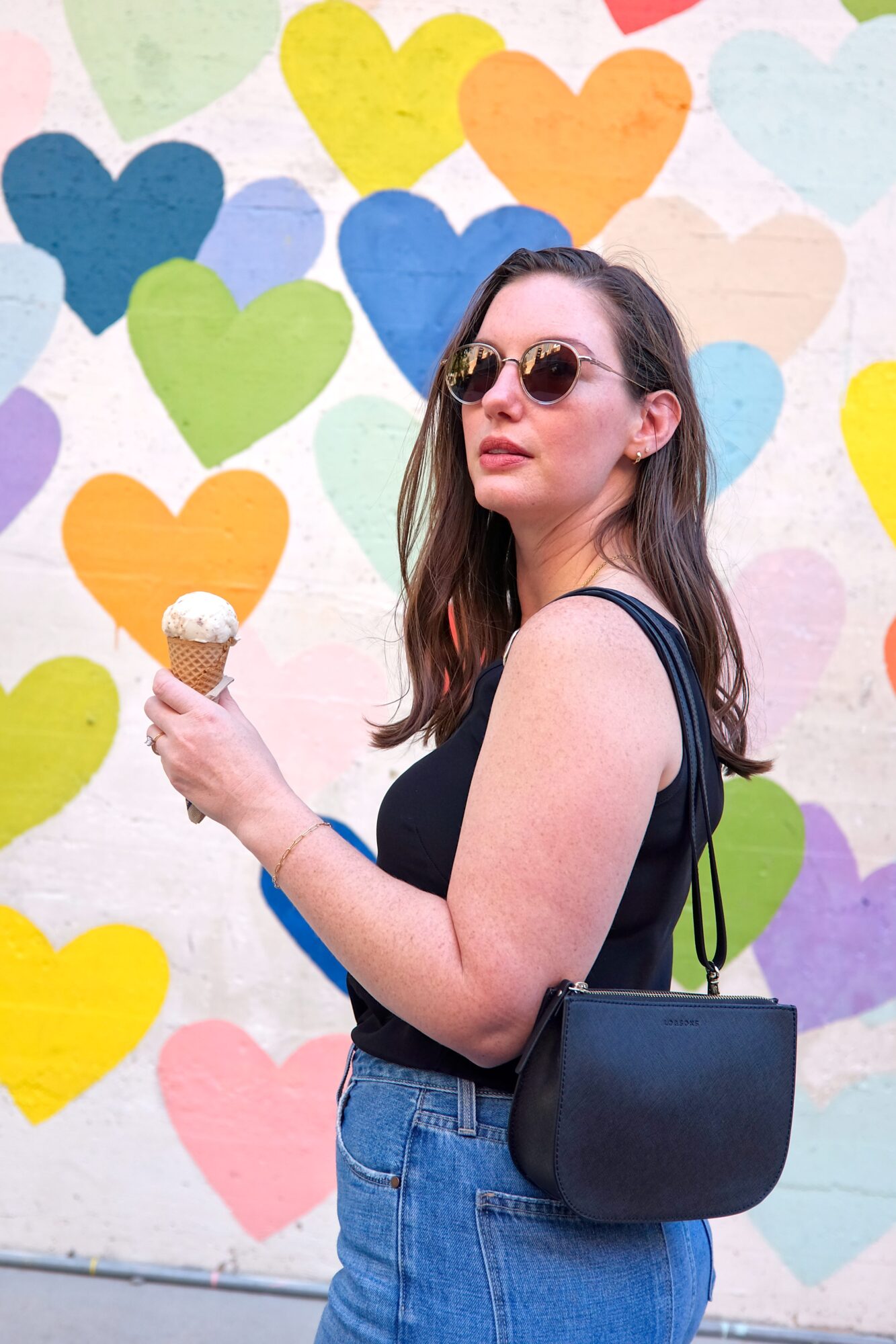 Alyssa holds an ice cream cone while wearing the Lo & Sons Waverley 2 Bag on her shoulder