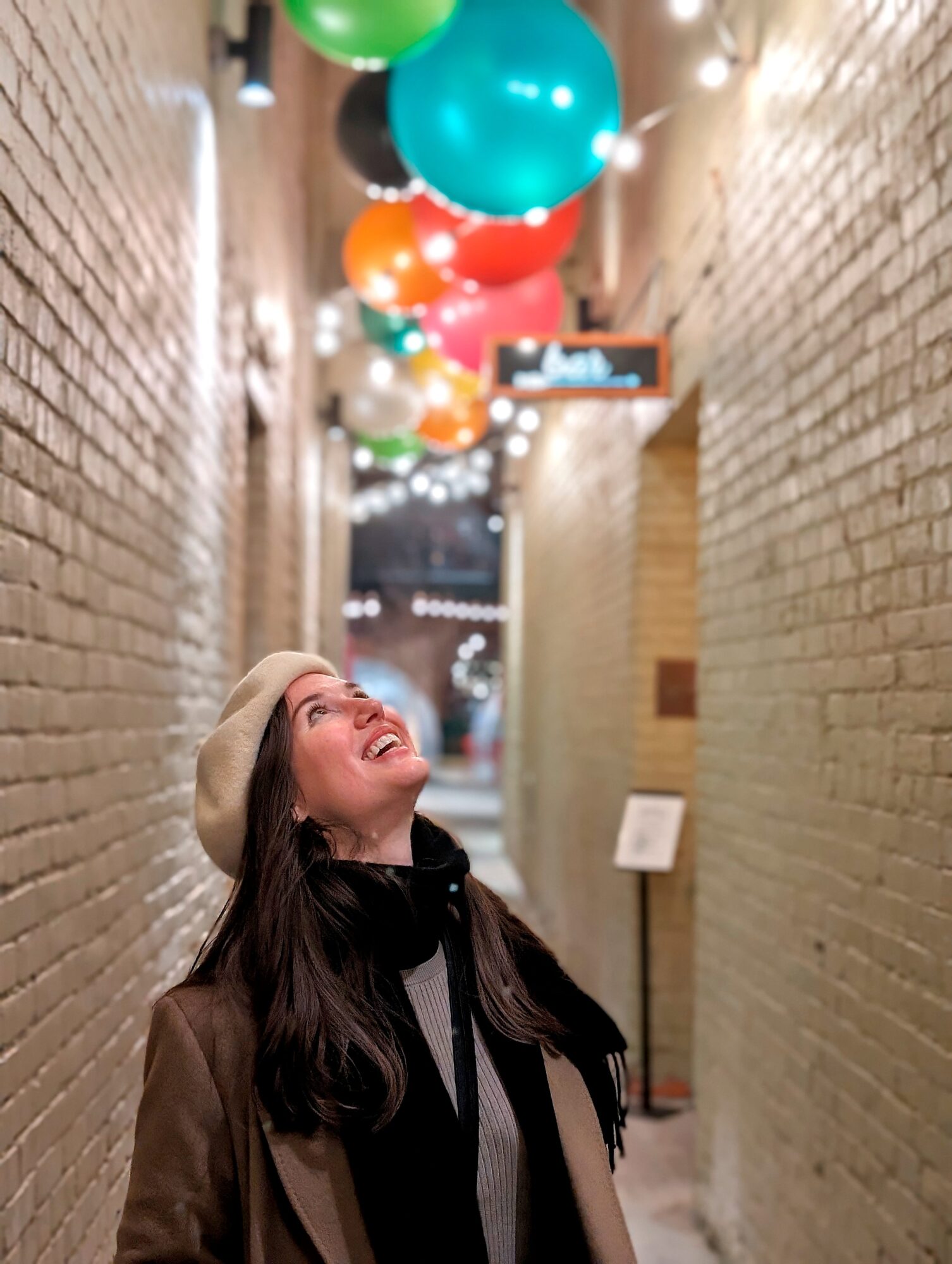 Alyssa looks up at bright balloons in an alley