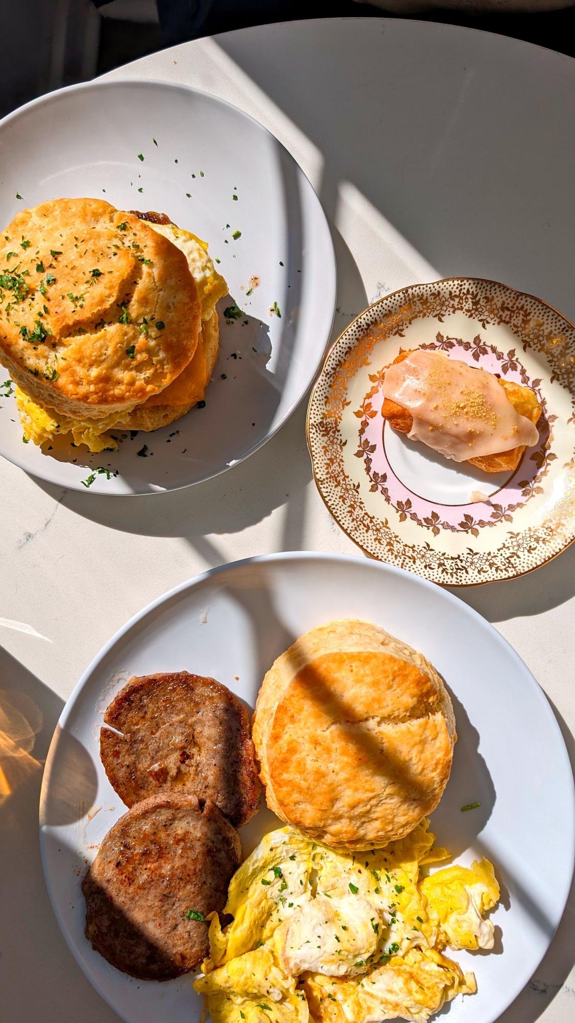 Biscuits, eggs, and sausage on a brightly lit table with a little pastry