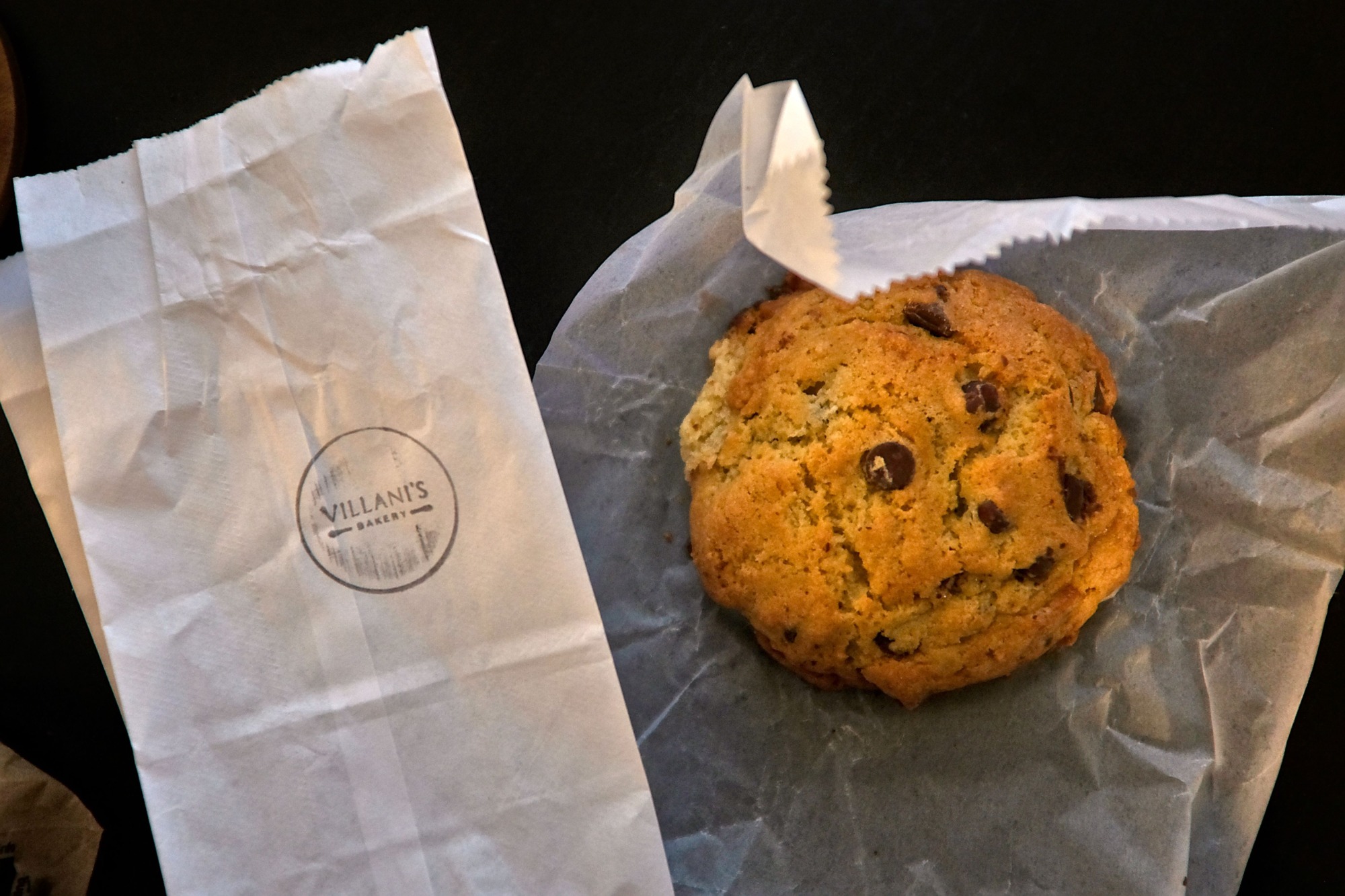 A chocolate chip cookie and a bag emblazoned with the Villani's Bakery logo