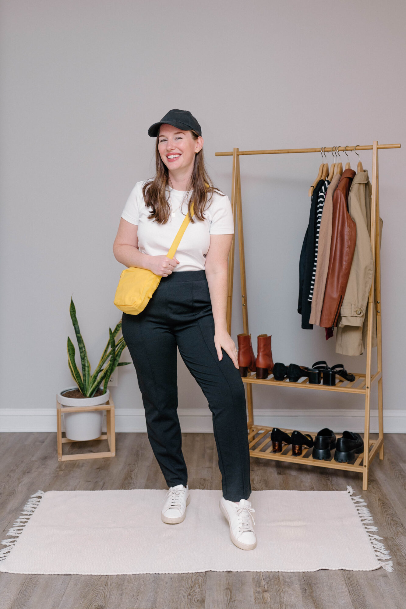 Alyssa wears the Rosso Straight Ponte Pant with a white tee, sneakers, yellow bag, and black cap