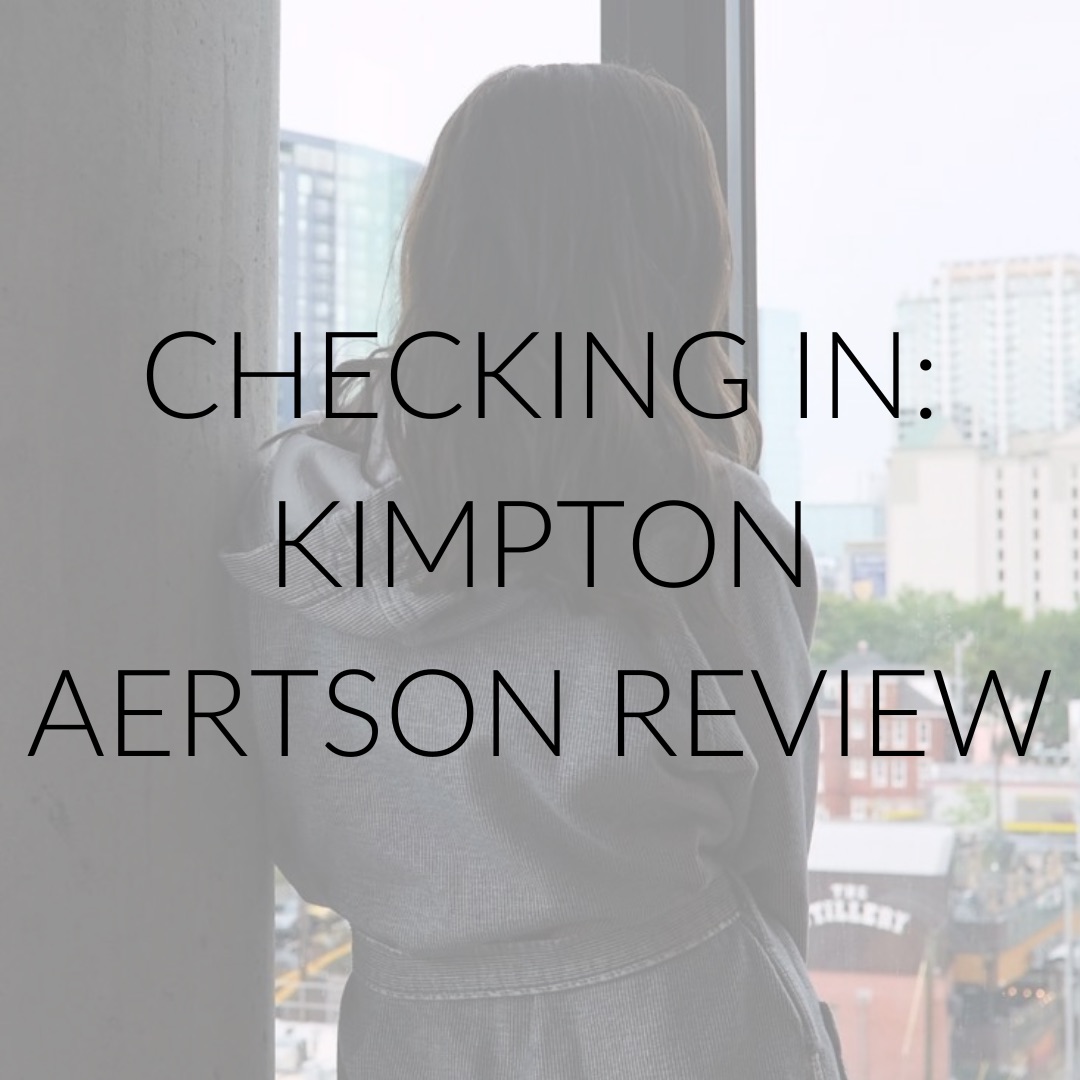 Alyssa wears a robe and looks out the window. Text overlay: Checking In: Kimpton Aertson Review