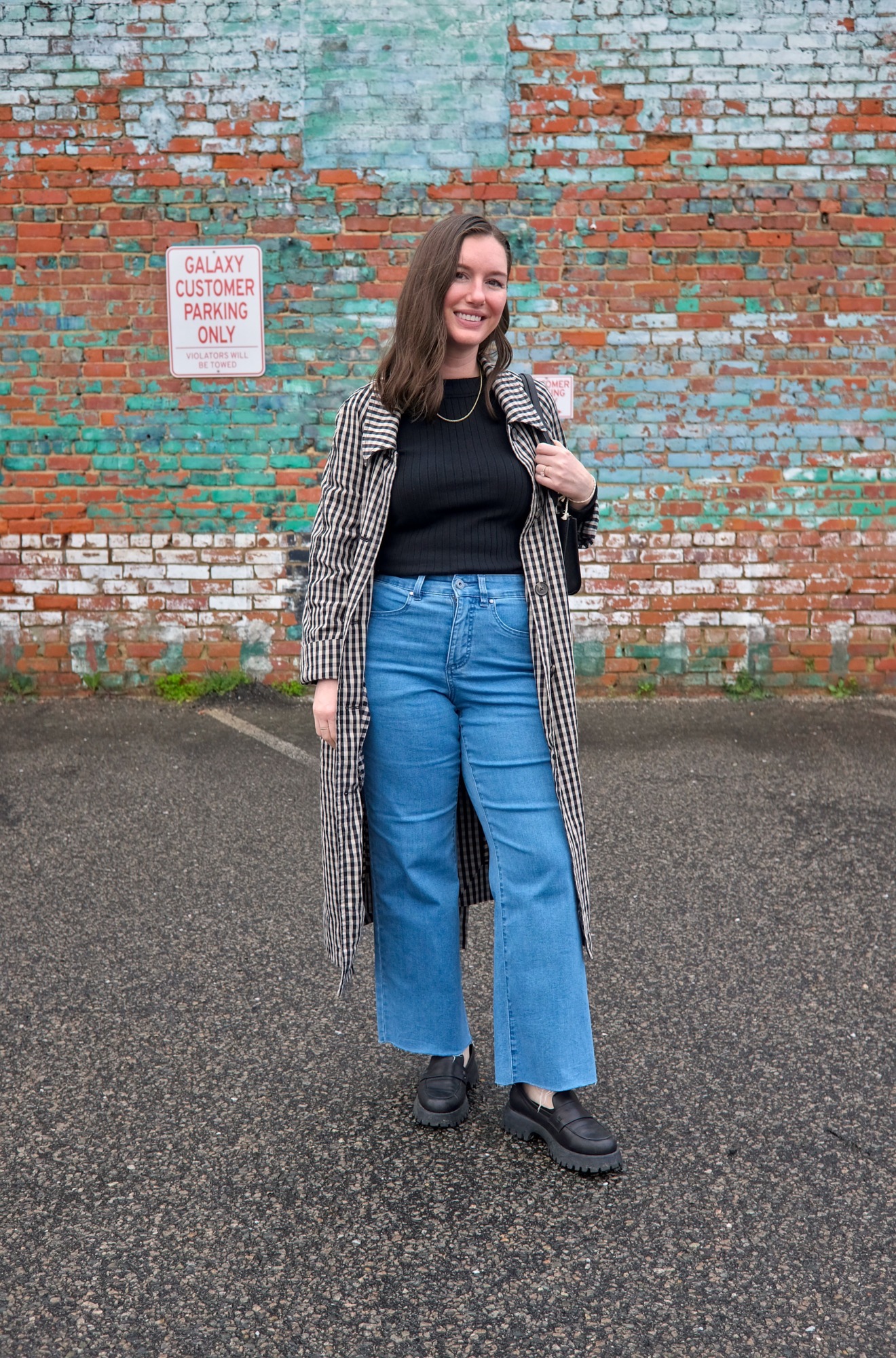 Alyssa wears a black top with blue jeans and a gingham trench