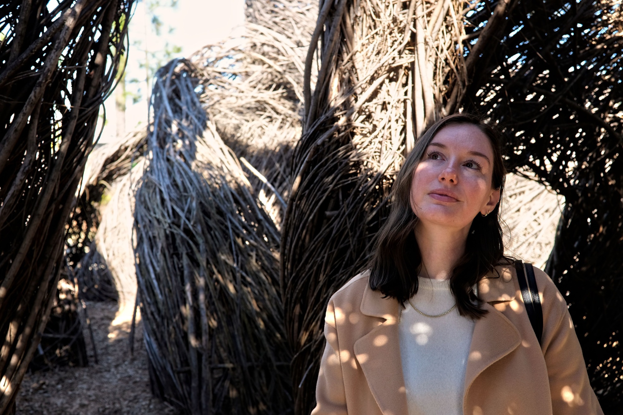 Alyssa stands in the shadows of a Patrick Dougherty sculpture