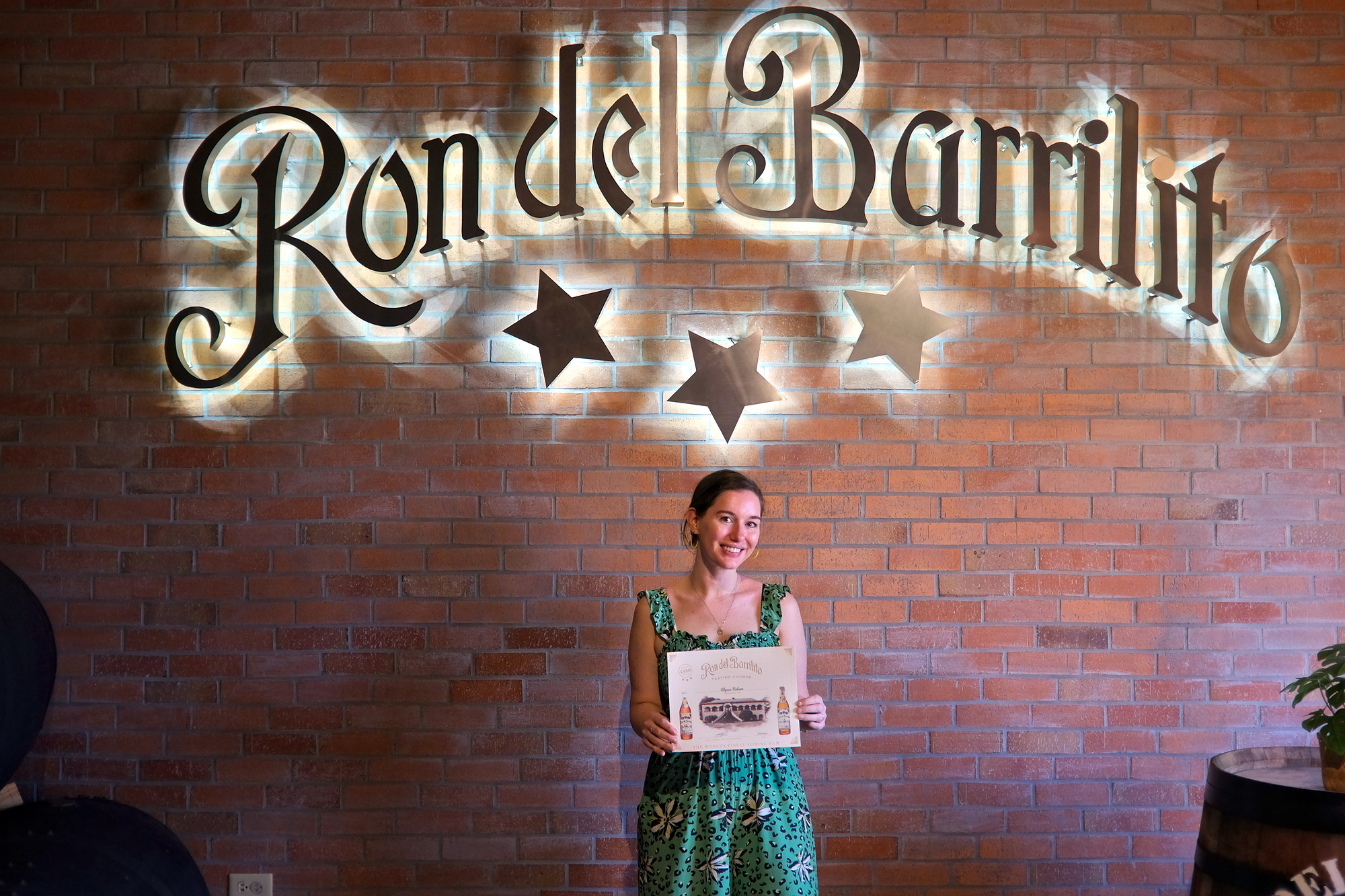 Alyssa holds a certificate in front of a Ron del Barrilito sign