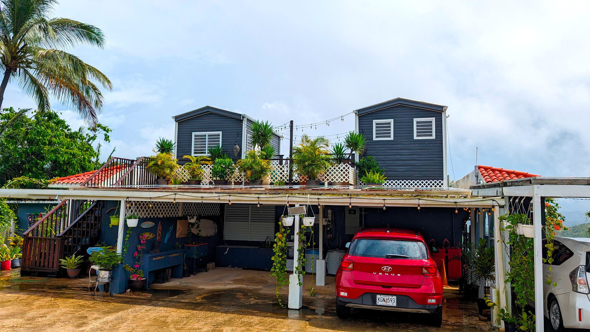 A red car underneath a carport topped with two tiny homes