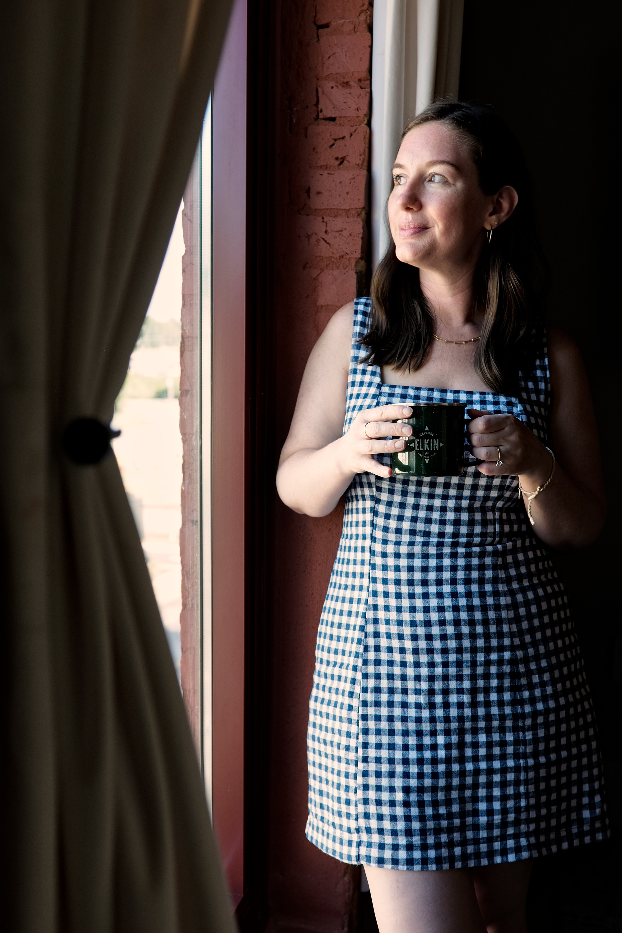 Alyssa holds a cup of coffee in the window at Three Trails