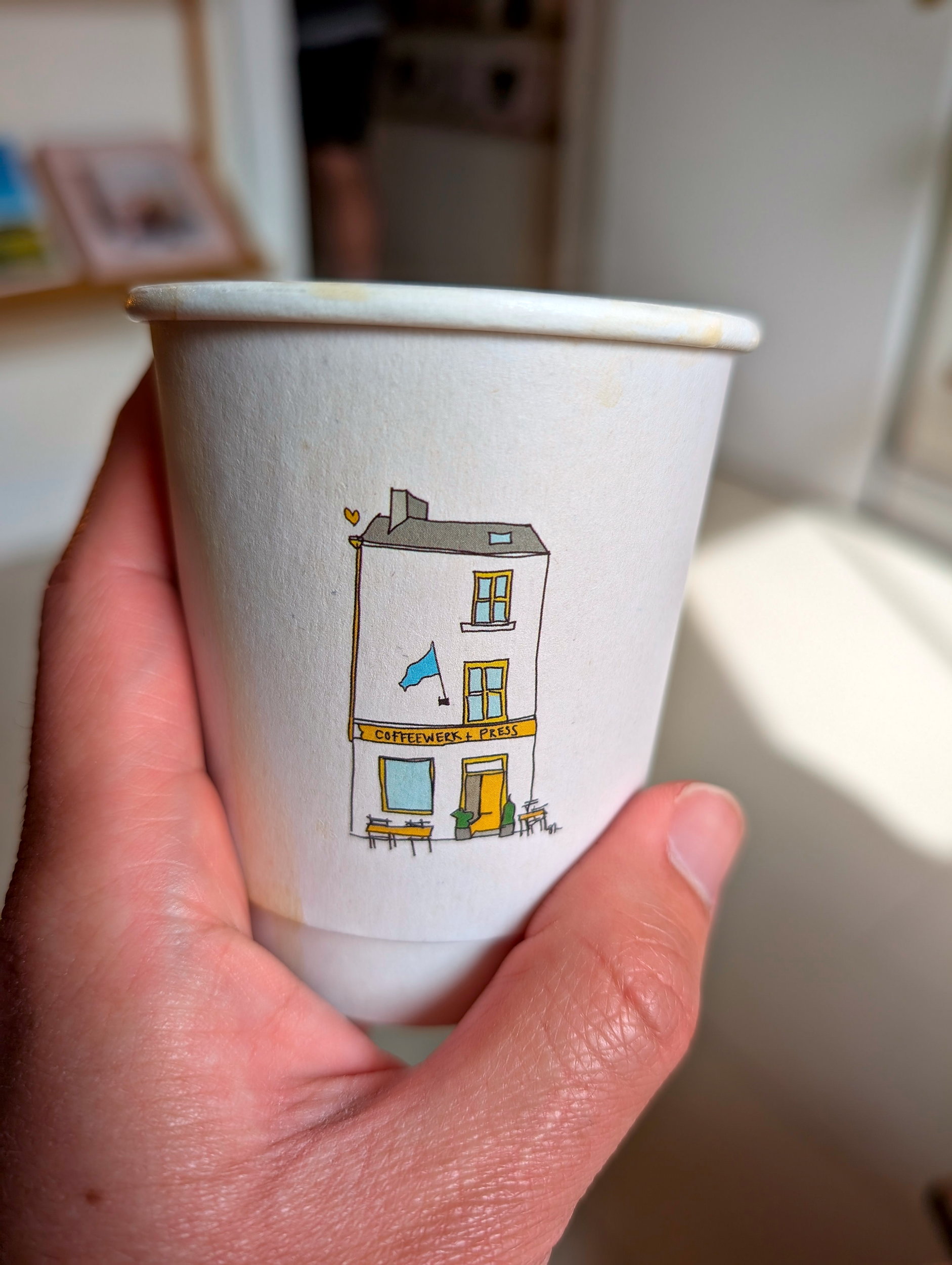 Simple white paper coffee cup from Coffeewerk + Press with a clean design, held by a hand, embodying the brand’s minimalist style.