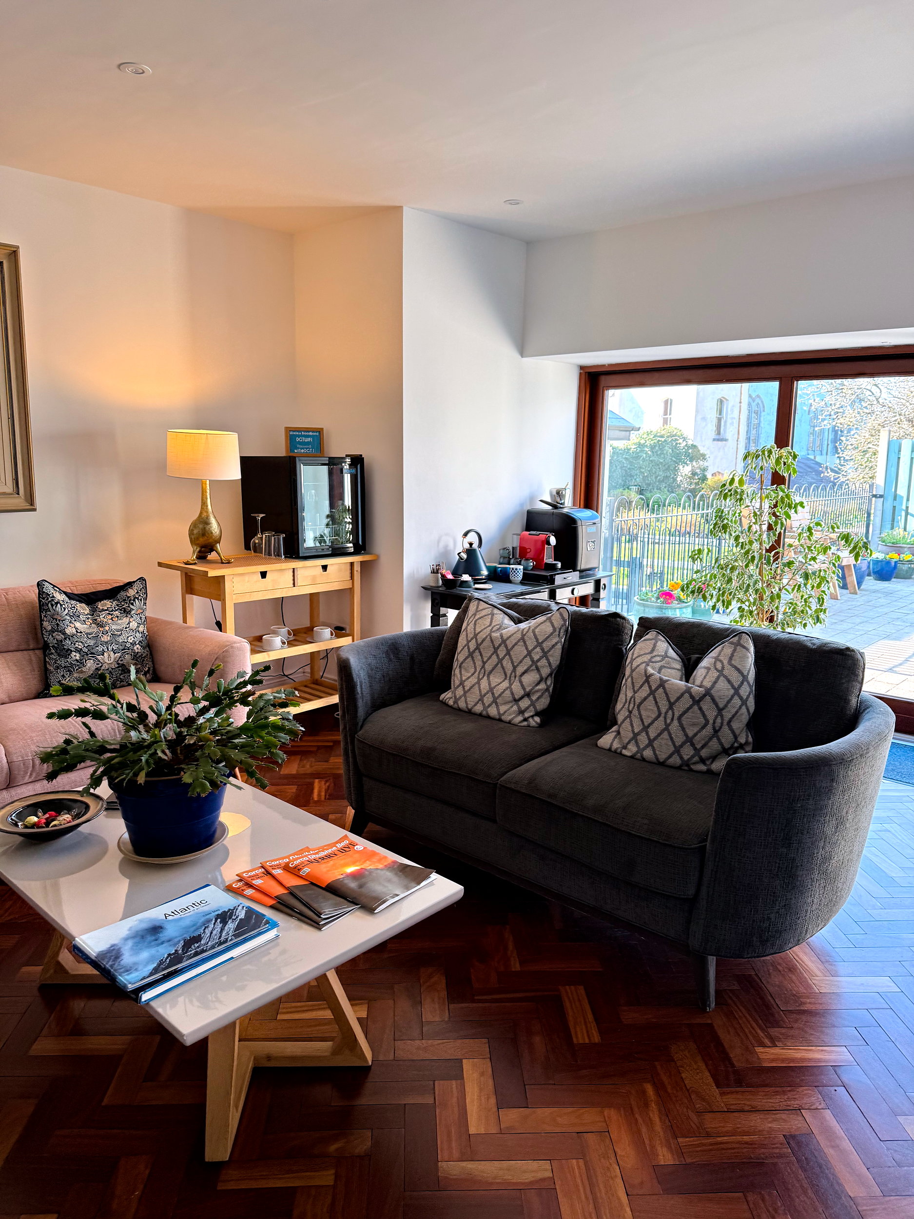 Bright, light-filled common area with cozy sofas, a coffee machine, and chilled water bottles set out for guests, creating a welcoming and relaxed space to unwind.