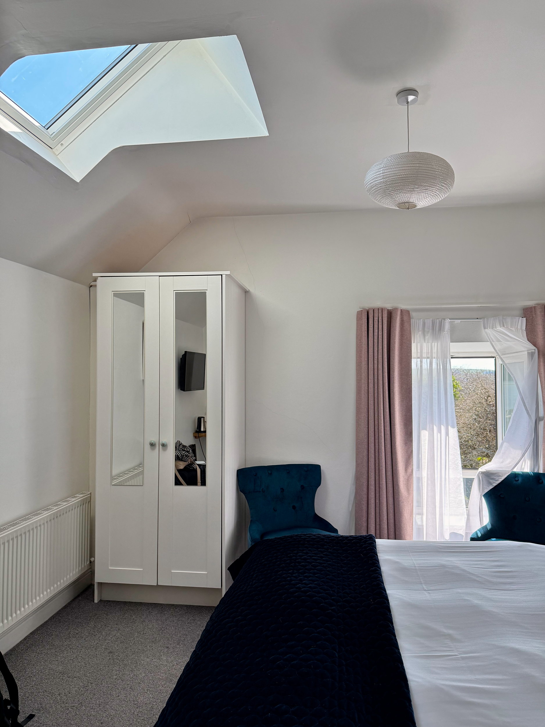 Bright and welcoming guest room at Dingle Garden Townhouse, featuring a cozy bed with white linens, modern decor, and soft natural light coming through the window.