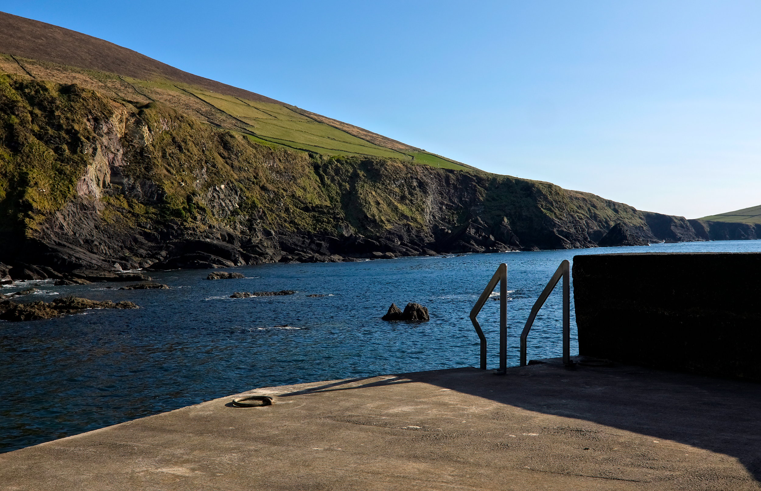 The bottom landing of Dunquin Pier, with a staircase and ramp that leads to the Atlantic and the rocky landscape in the background