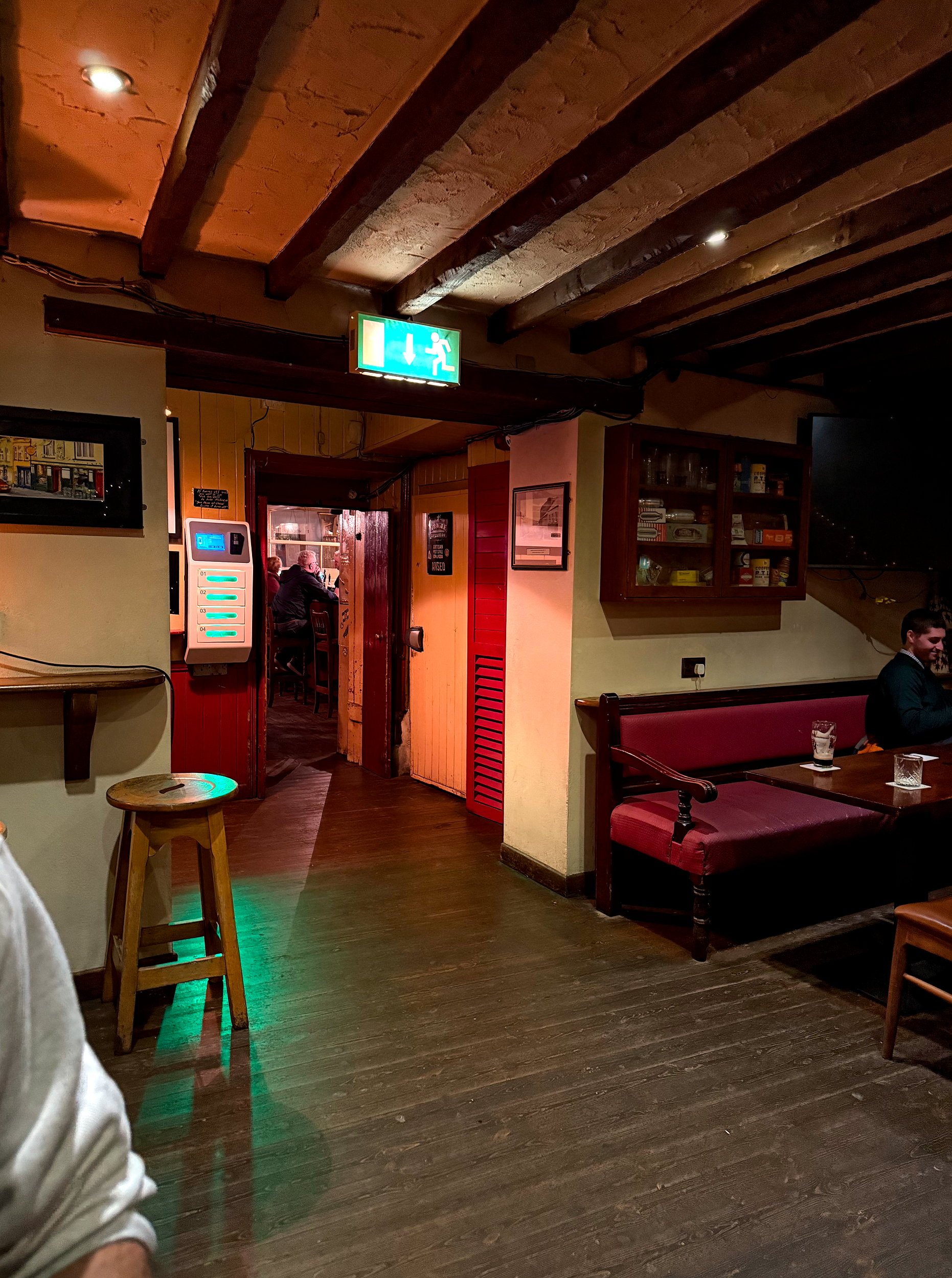 Cozy seating area at Foxy John’s with the bar in the background, featuring a classic wooden counter, barstools, and pint glasses, with hardware merchandise visible nearby, capturing the pub’s unique dual-purpose vibe.