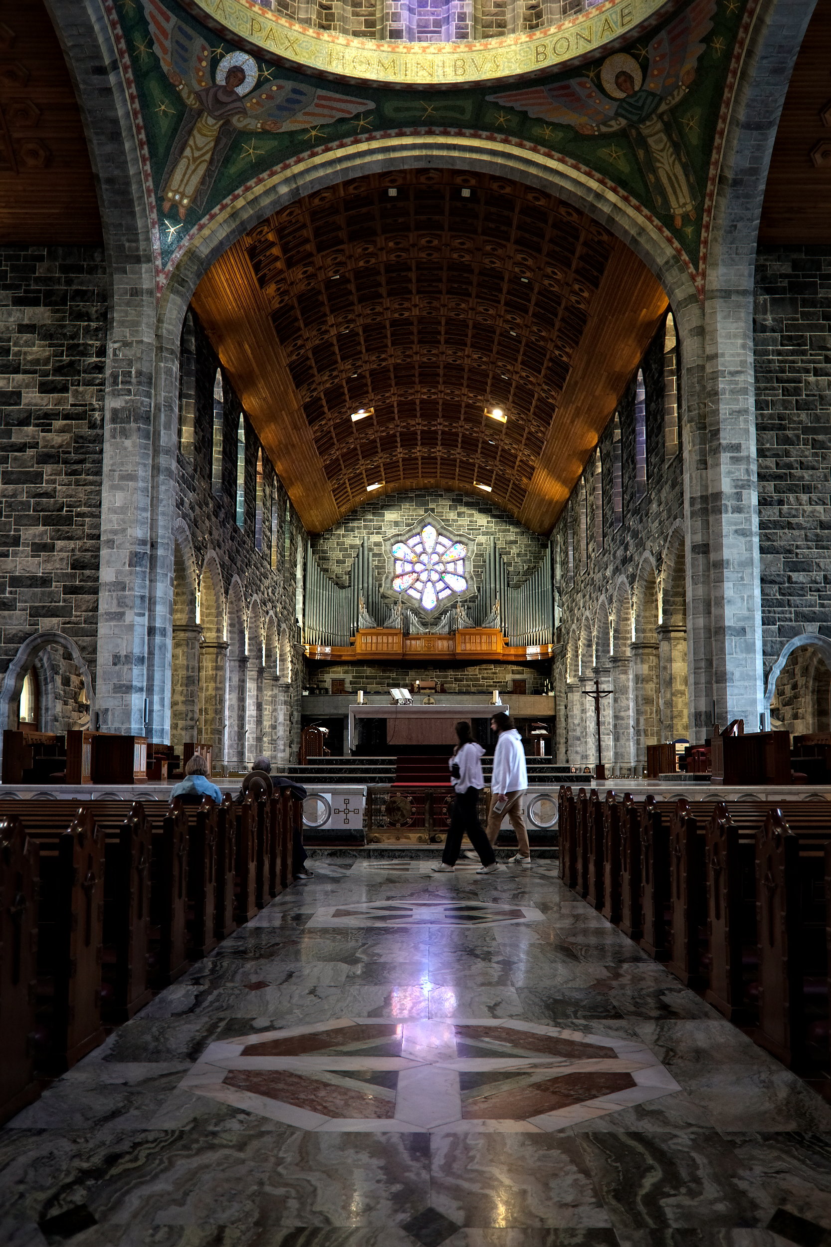 Interior shot of Galway Cathedral showcasing its high vaulted ceilings, stained glass windows casting colorful light, and intricate stone and woodwork leading toward the altar.