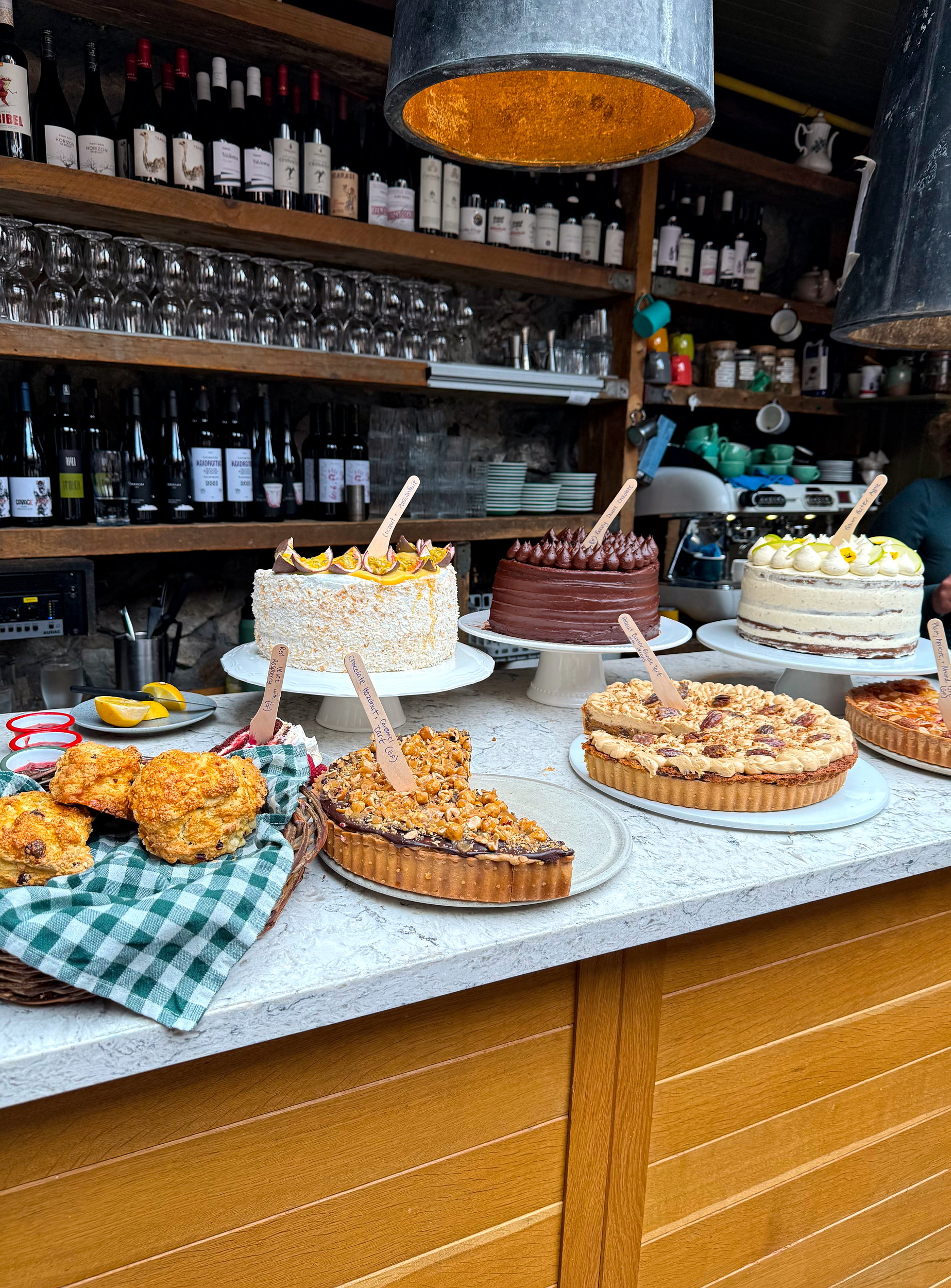 Rustic wooden bar at Kai Restaurant, covered with an inviting assortment of homemade cakes, pies, and tarts displayed on vintage cake stands.