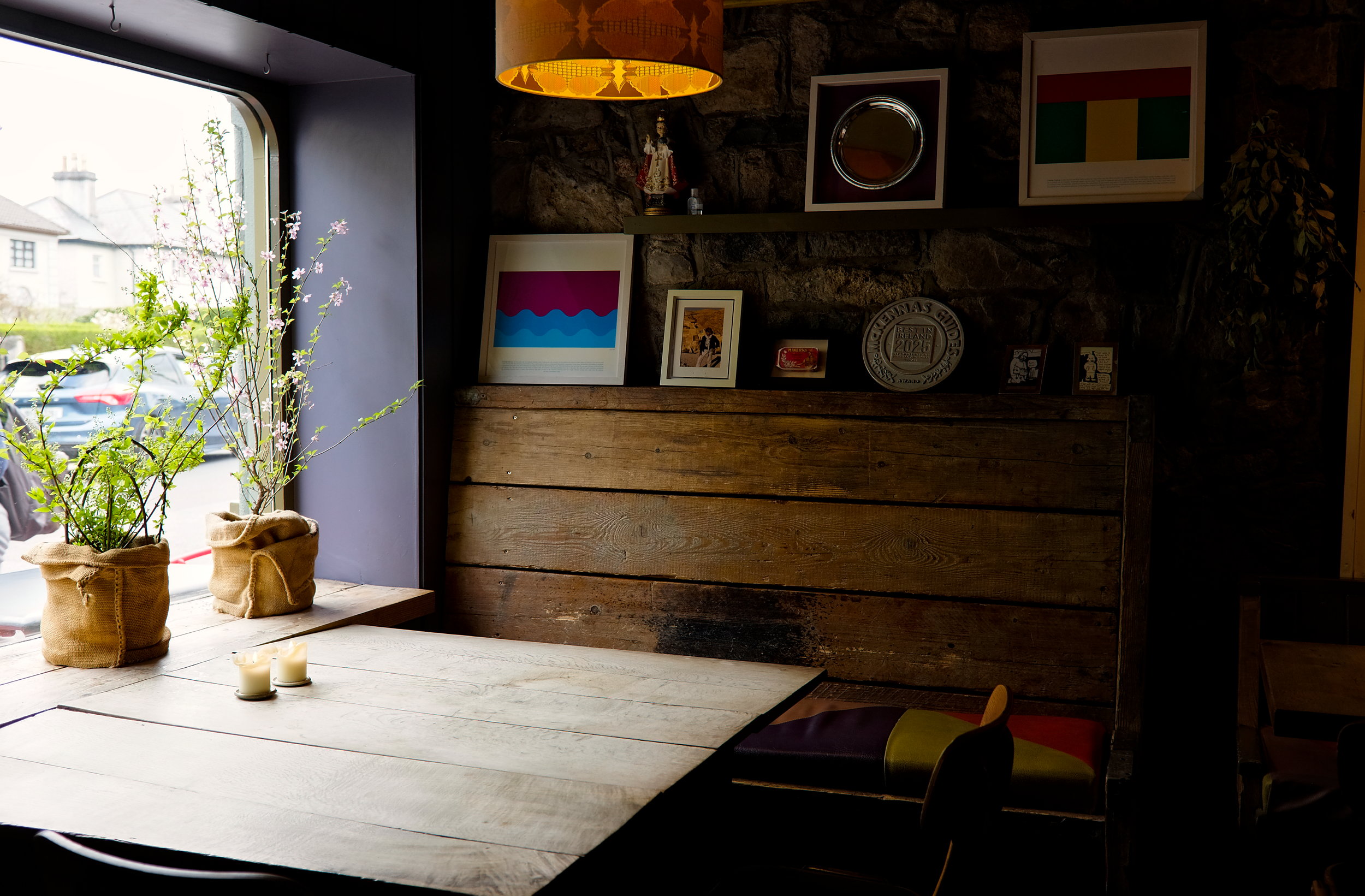 Cozy interior of Kai Restaurant in Galway featuring a rustic wooden booth, textured walls, dried flowers, and warm natural light streaming in through large windows.