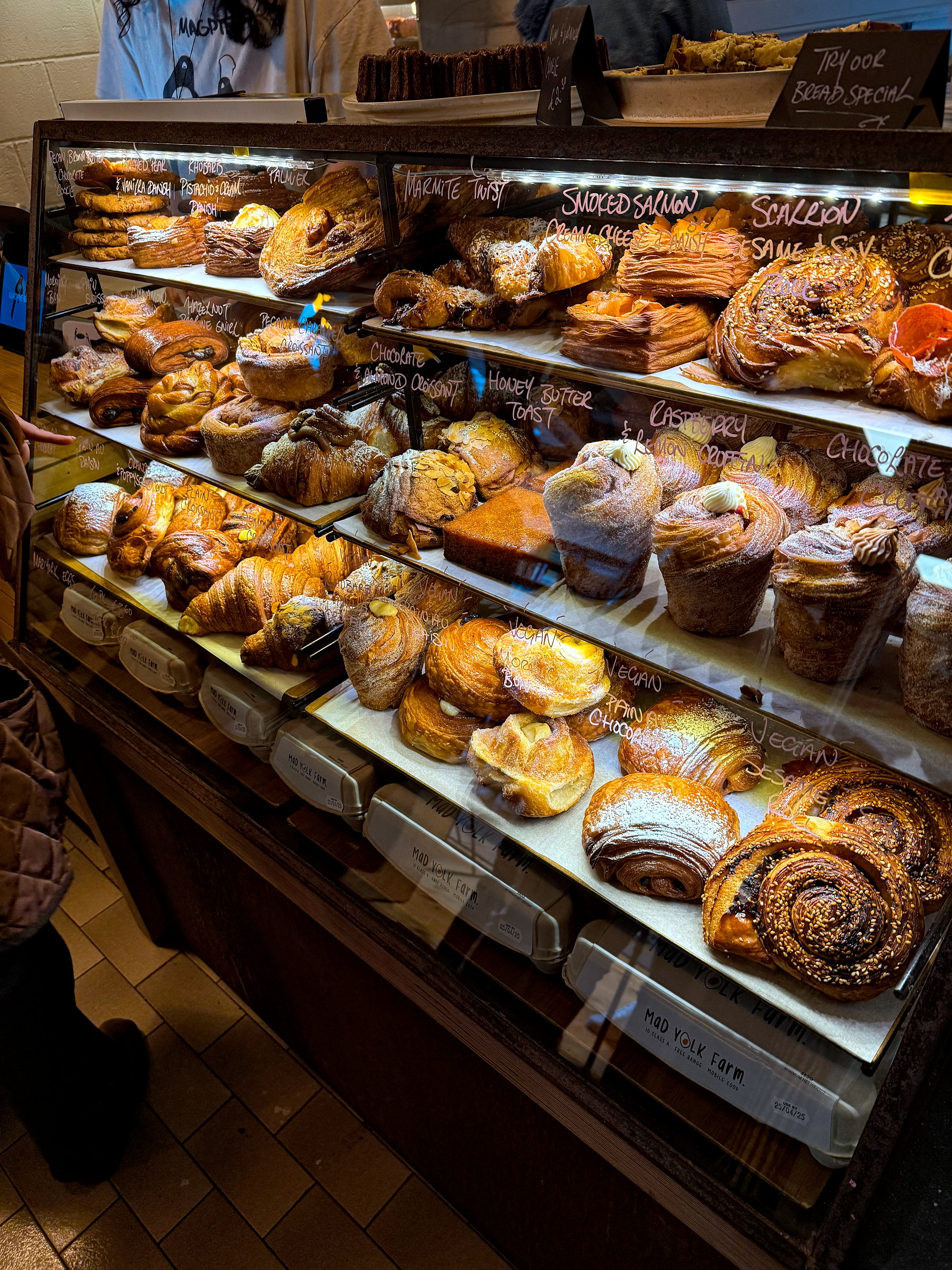 Glass pastry case at Magpie Bakery filled with an assortment of golden, flaky pastries including croissants, danishes, and tarts, all neatly arranged on trays under soft lighting.