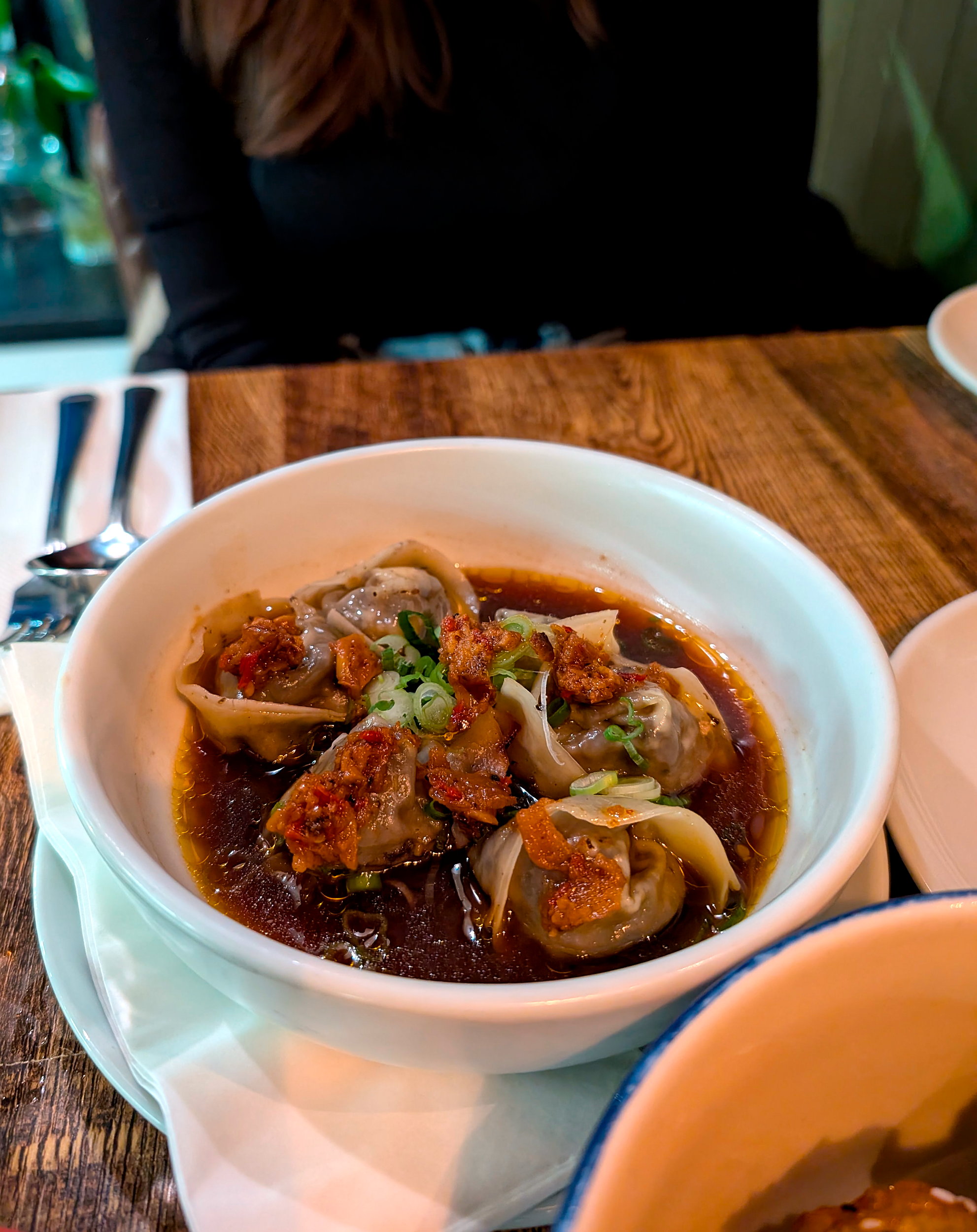 Shallow ceramic bowl filled with delicate, golden-brown dumplings at Rúibín, garnished with scallions and swimming in a savory sauce.