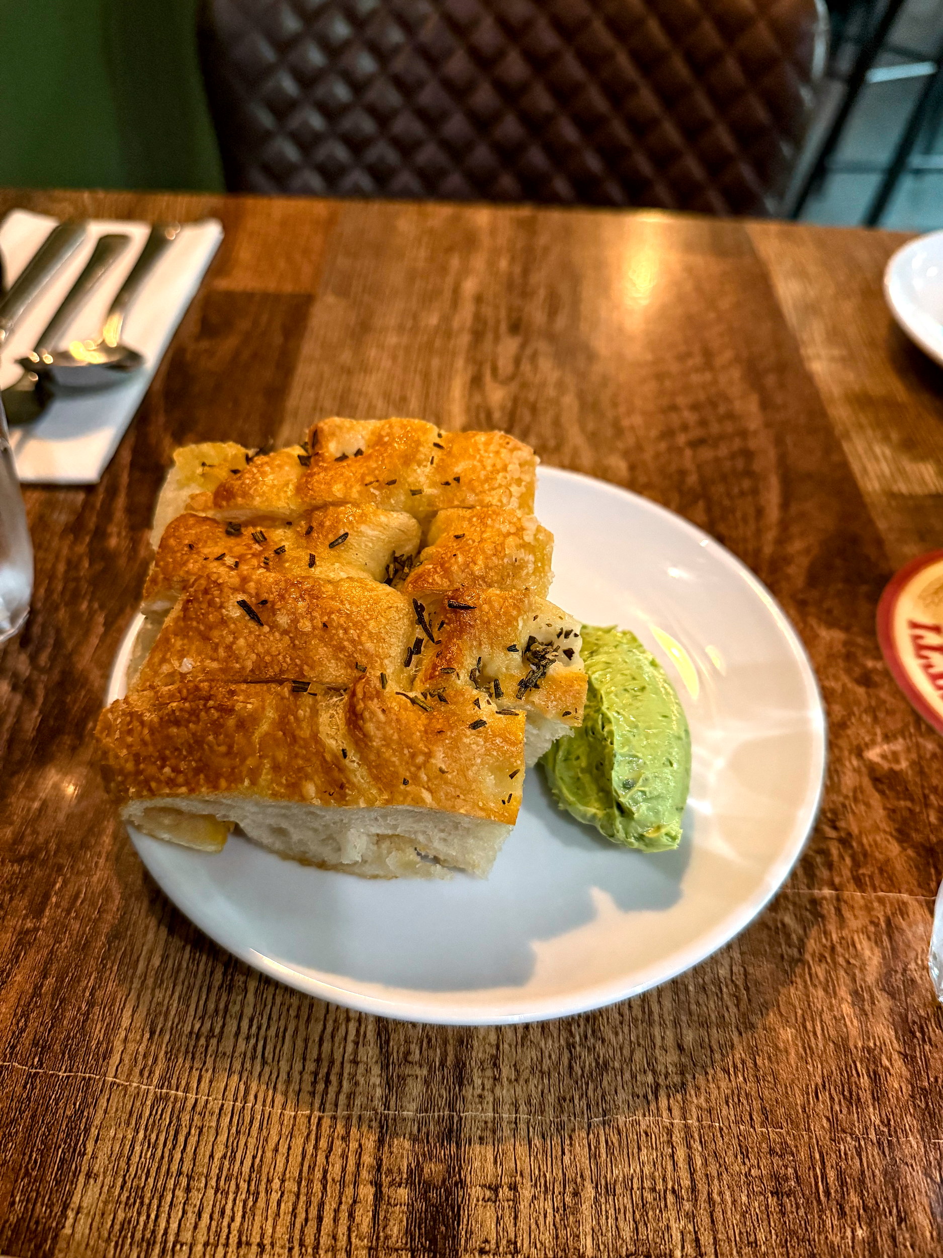 Close-up of a white plate with thick slices of golden, airy focaccia served alongside a quenelle of vibrant green herb butter at Rúibín.