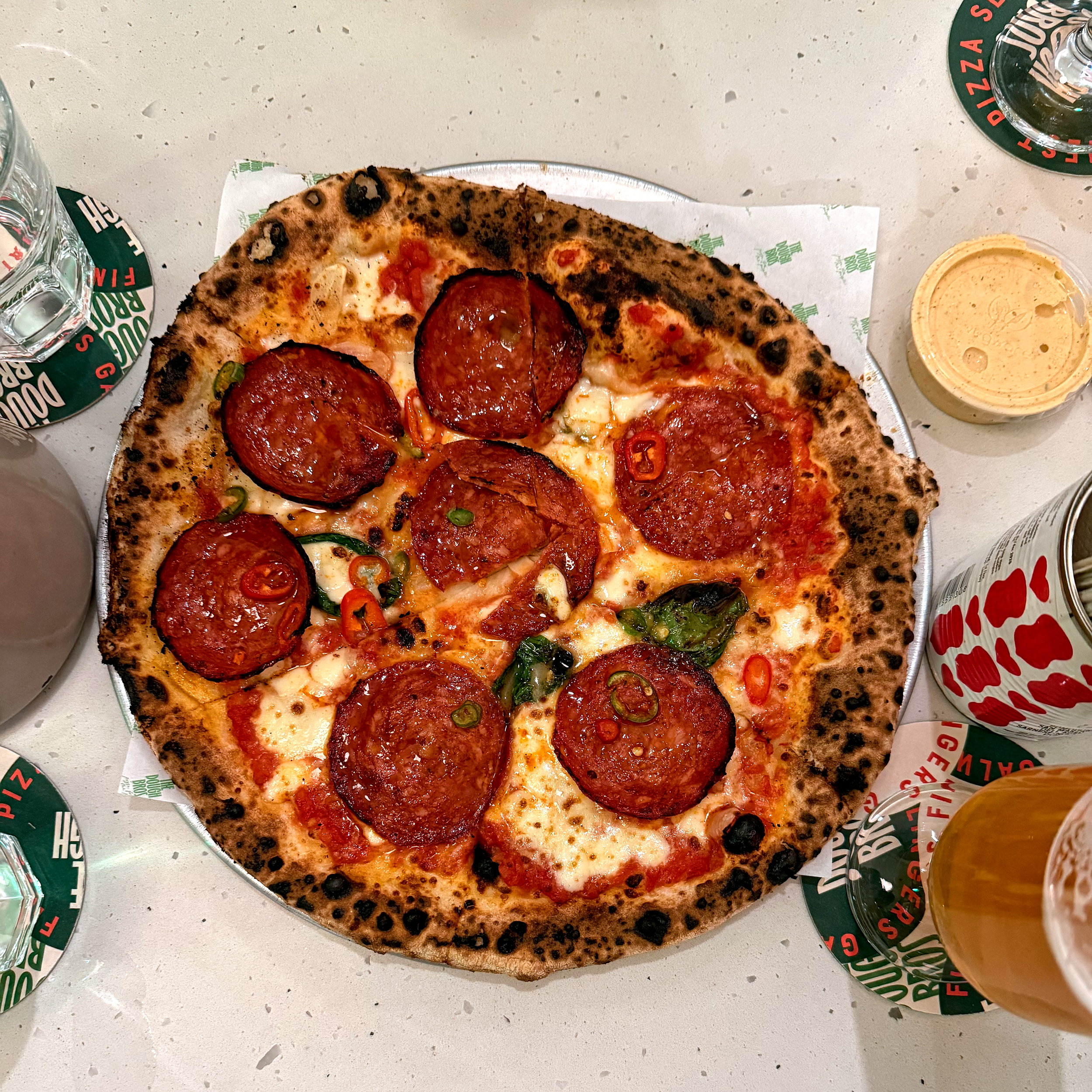 Close-up of a freshly baked pizza topped with large rounds of spicy chorizo, melted mozzarella, and a blistered, wood-fired crust on a metal plate.