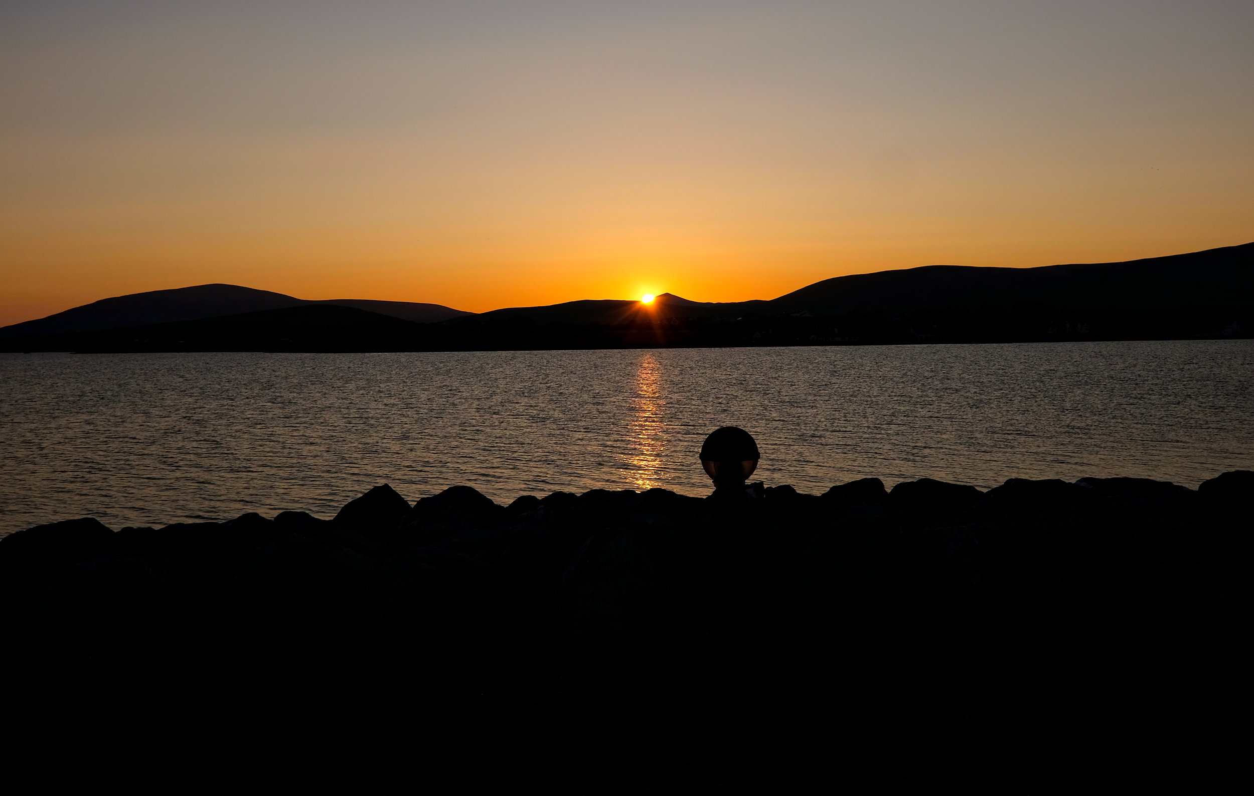 Golden sunset casting a warm glow over Dingle Harbor, with the sun dipping behind the hills