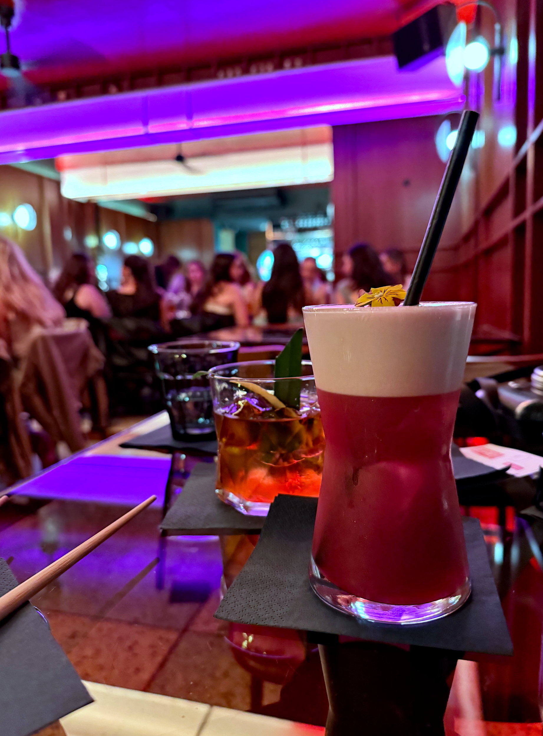 Two cocktails on a table with a busy dining room at BIGFAN in the background