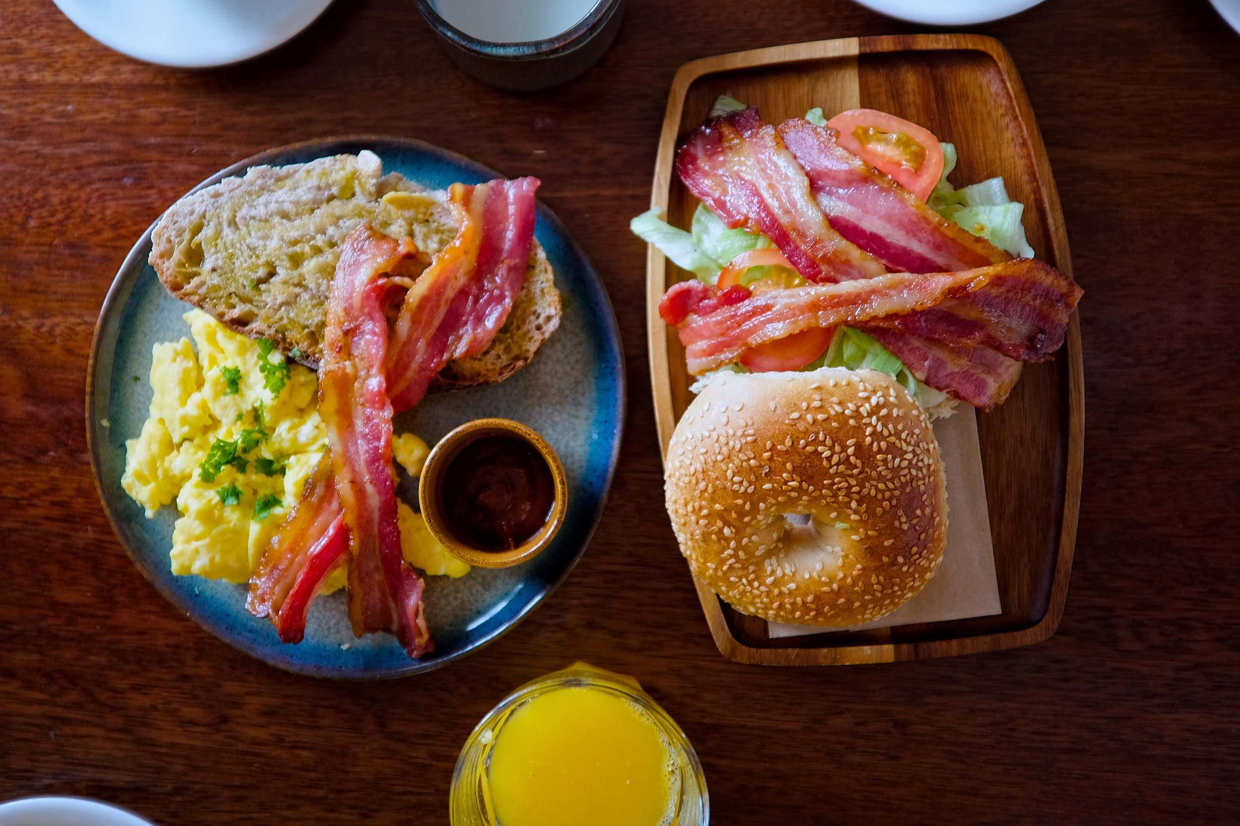 A bagel BLT and a plate of scrambled eggs, bacon, and toast from The Stop's breakfast menu, along with homemade granola and cake