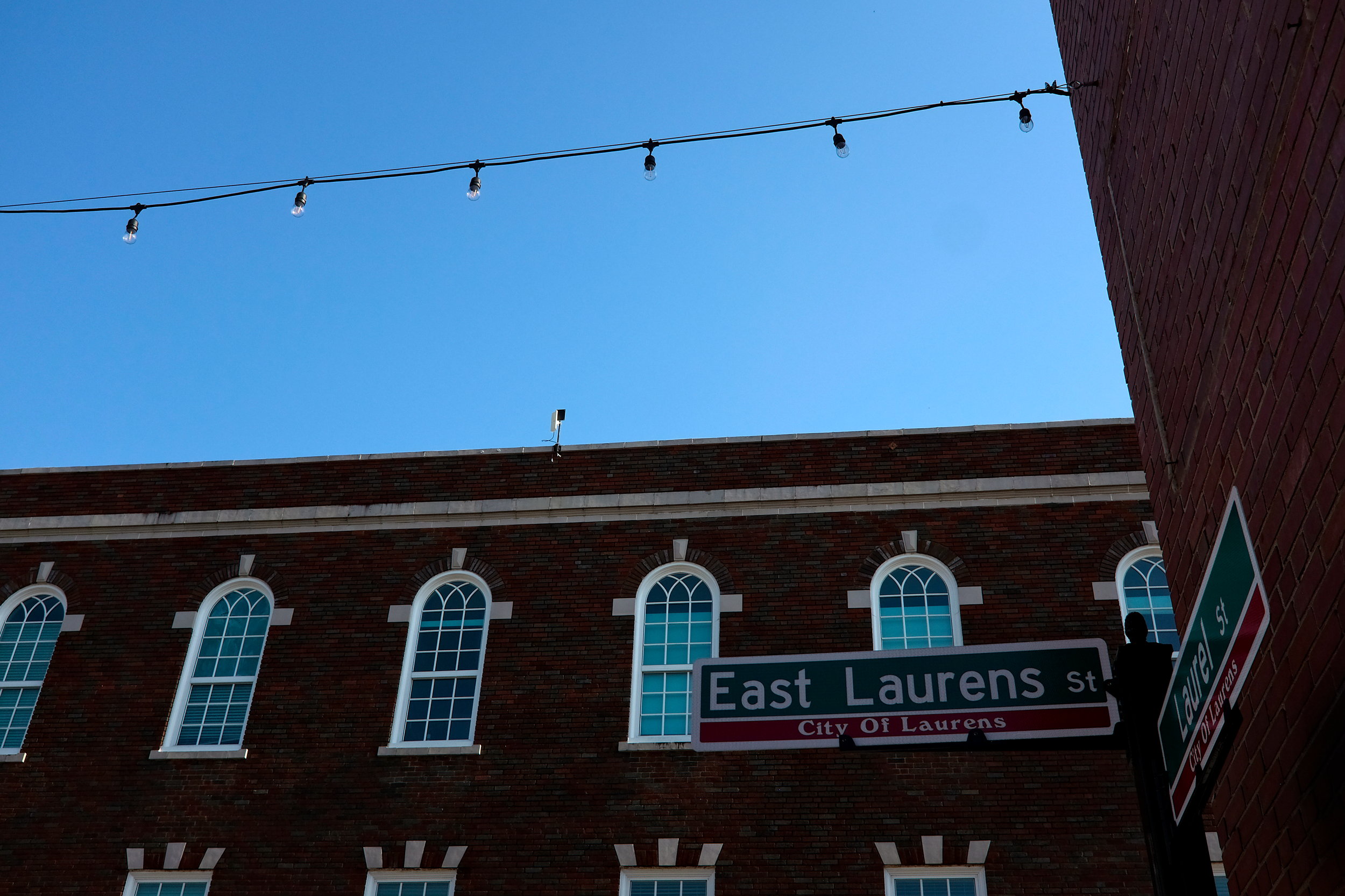 A street sign that reads "East Laurens St" in front of a brick building in Laurens, SC