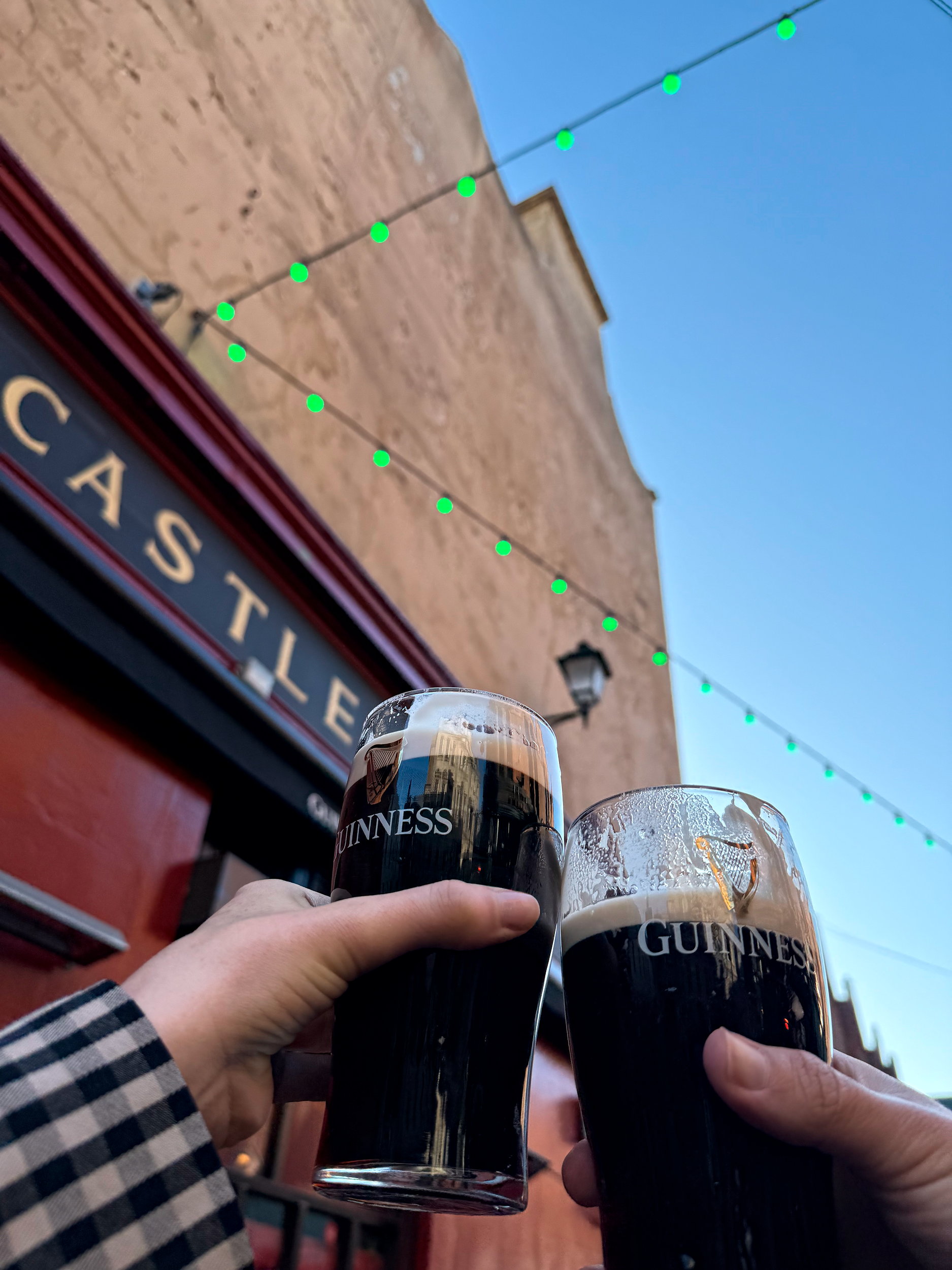 Two hands hold a pair of Guinness pints and toast in front of Grogan's Castle Lounge in Dublin, Ireland