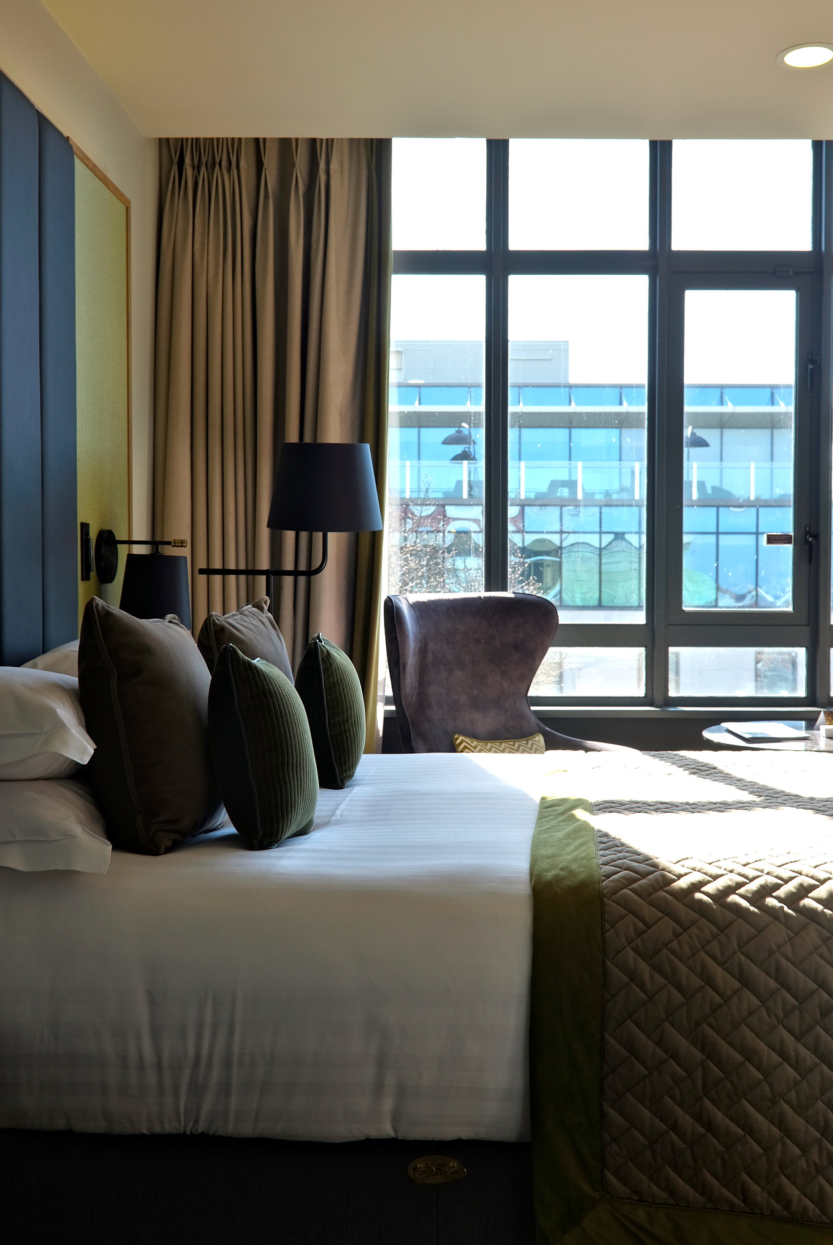 A king bed in the foreground with floor to ceiling windows overlooking Dublin in the background