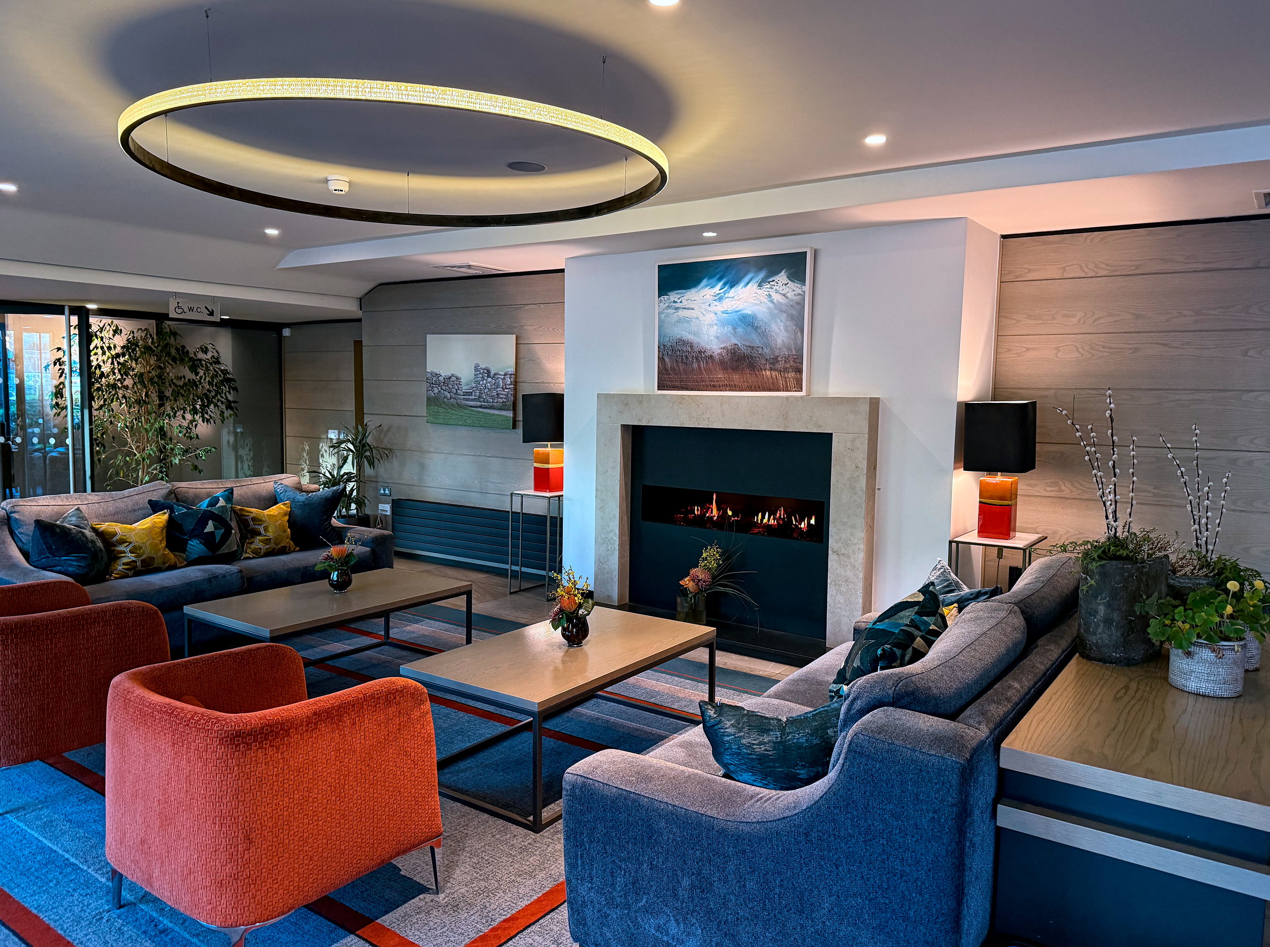A colorful lobby at Mespil Hotel, with a fireplace, sofas, coffee tables, and circular light fixture