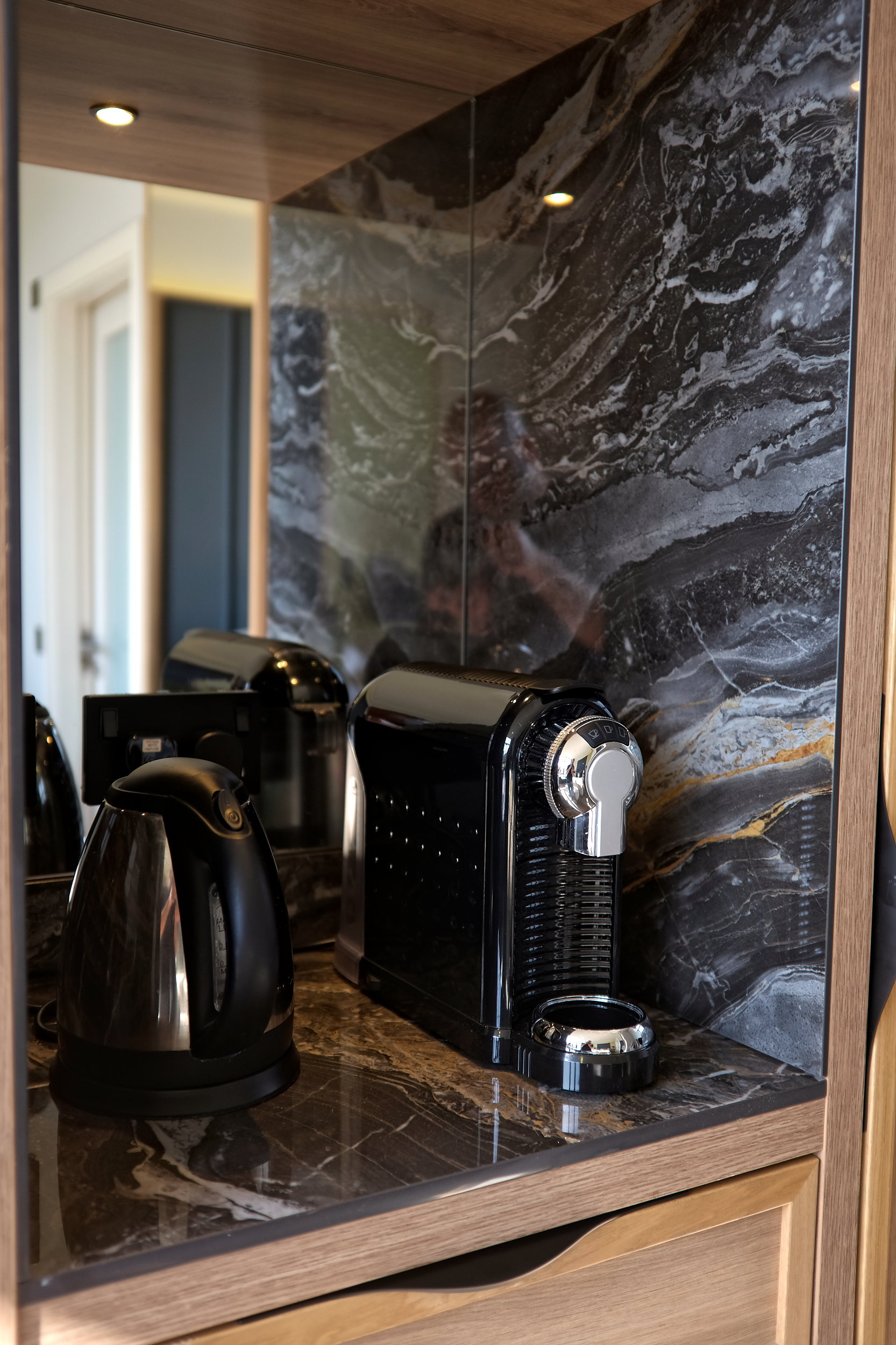 A Nespresso machine and tea kettle on a marble lined stand in the hotel room