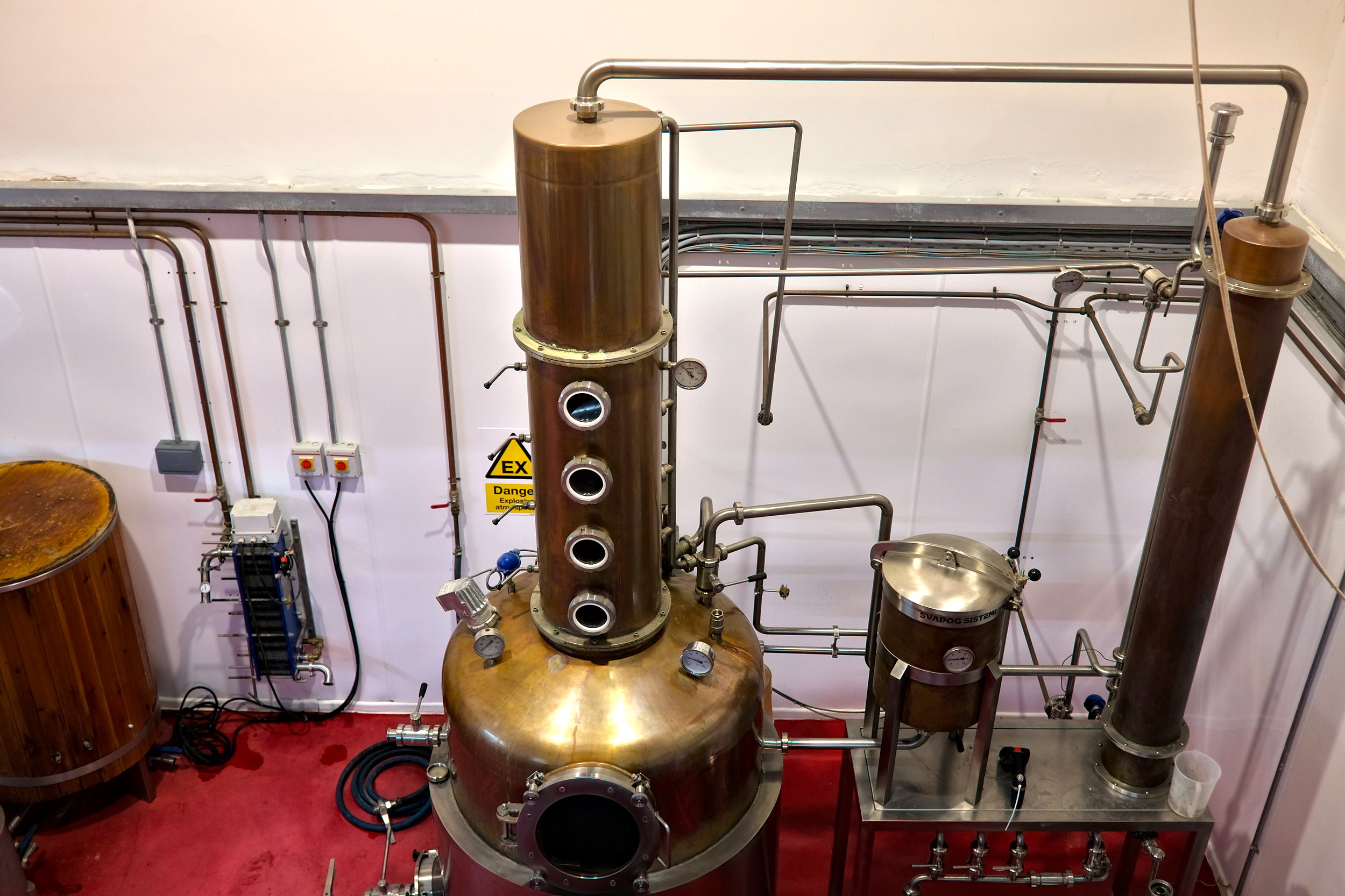 Overhead view of copper distillation equipment at Micil Distillery, with pipes, stills, and tanks arranged in a compact space that blends industrial function with artisanal craft.