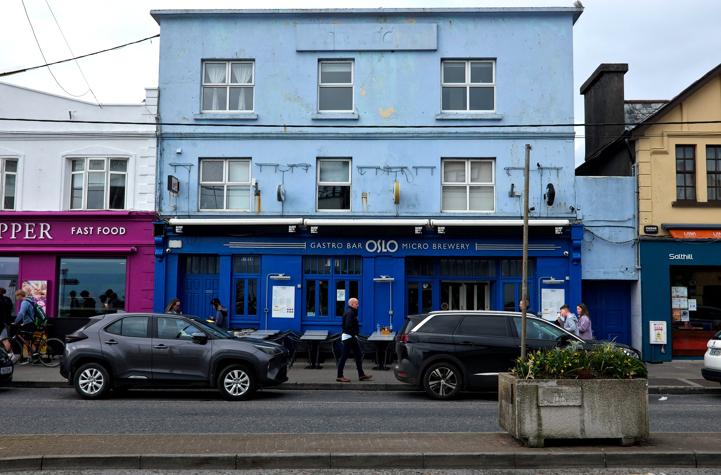 Street view of the Oslo Bar in Galway, home to Micil Distillery, with its blue façade, large front windows, and the Micil logo subtly displayed on barrels, capturing a blend of modern craft and traditional pub charm.