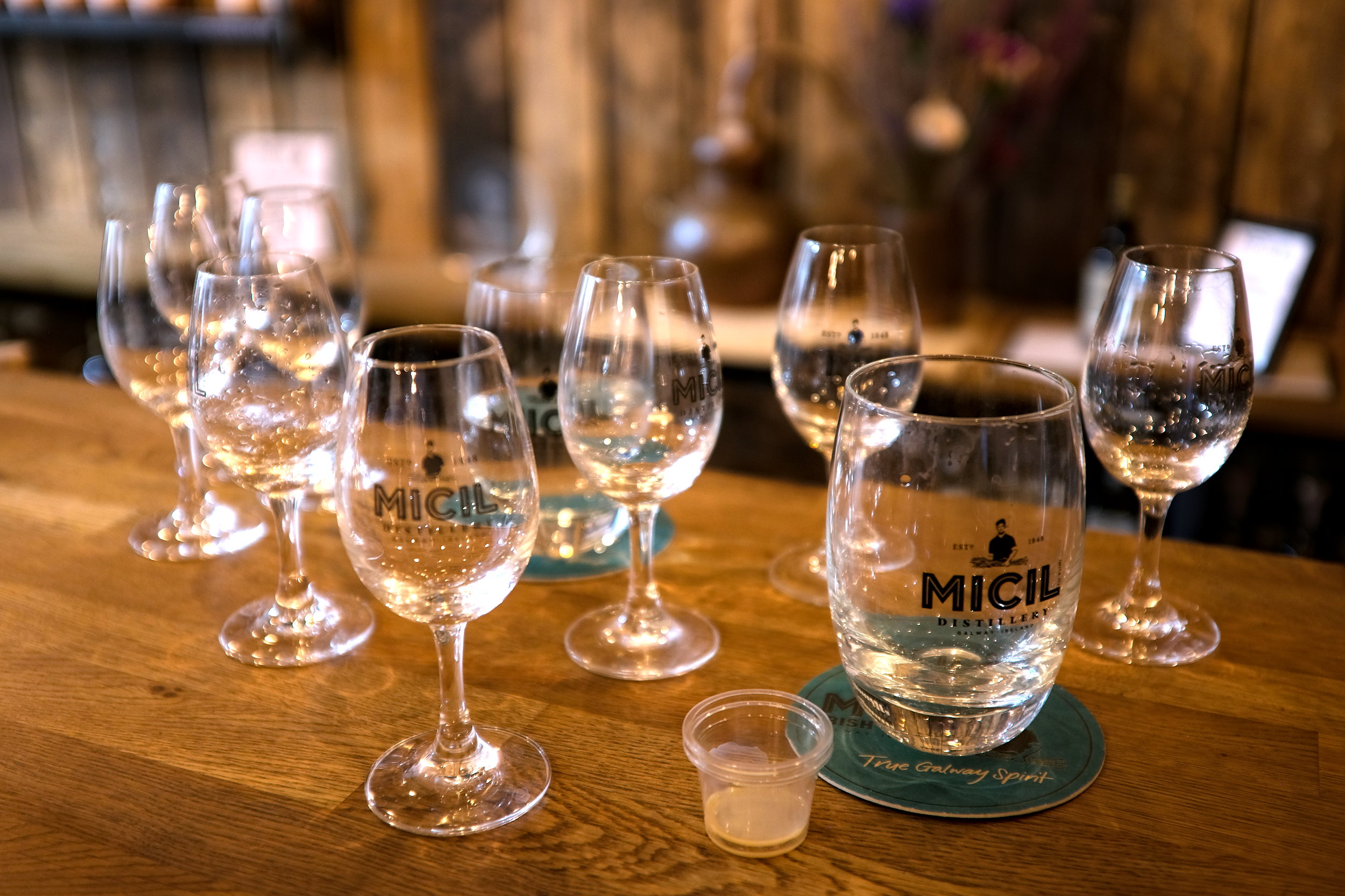 Table scattered with empty whiskey tasting glasses at Micil Distillery, some with traces of golden liquid, reflecting the end of a guided tasting session.