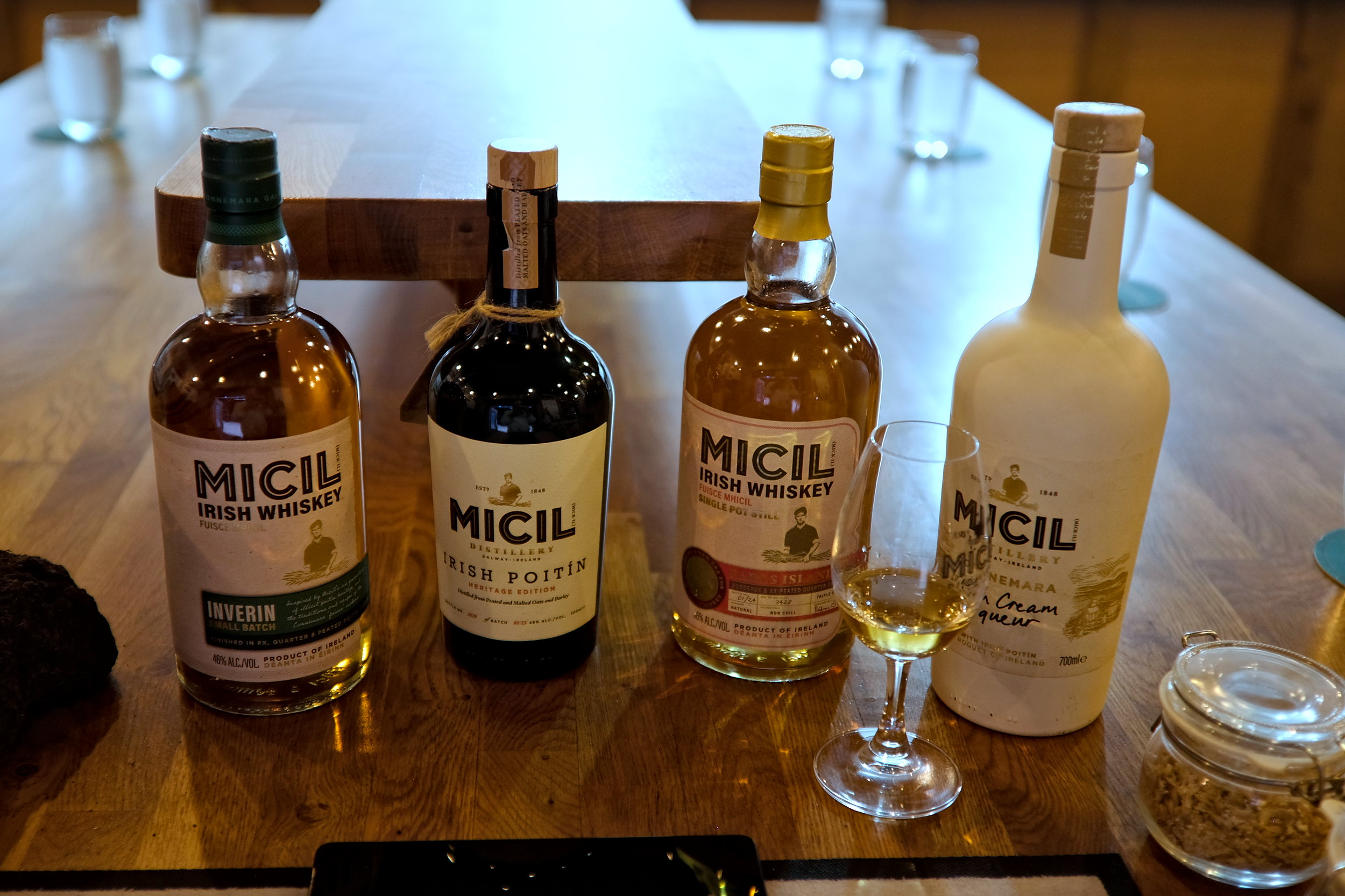 Product lineup featuring two bottles of Micil whiskey, a clear bottle of poitín, and a sleek bottle of Micil Irish cream, all set against a neutral background to highlight the branding and labels.