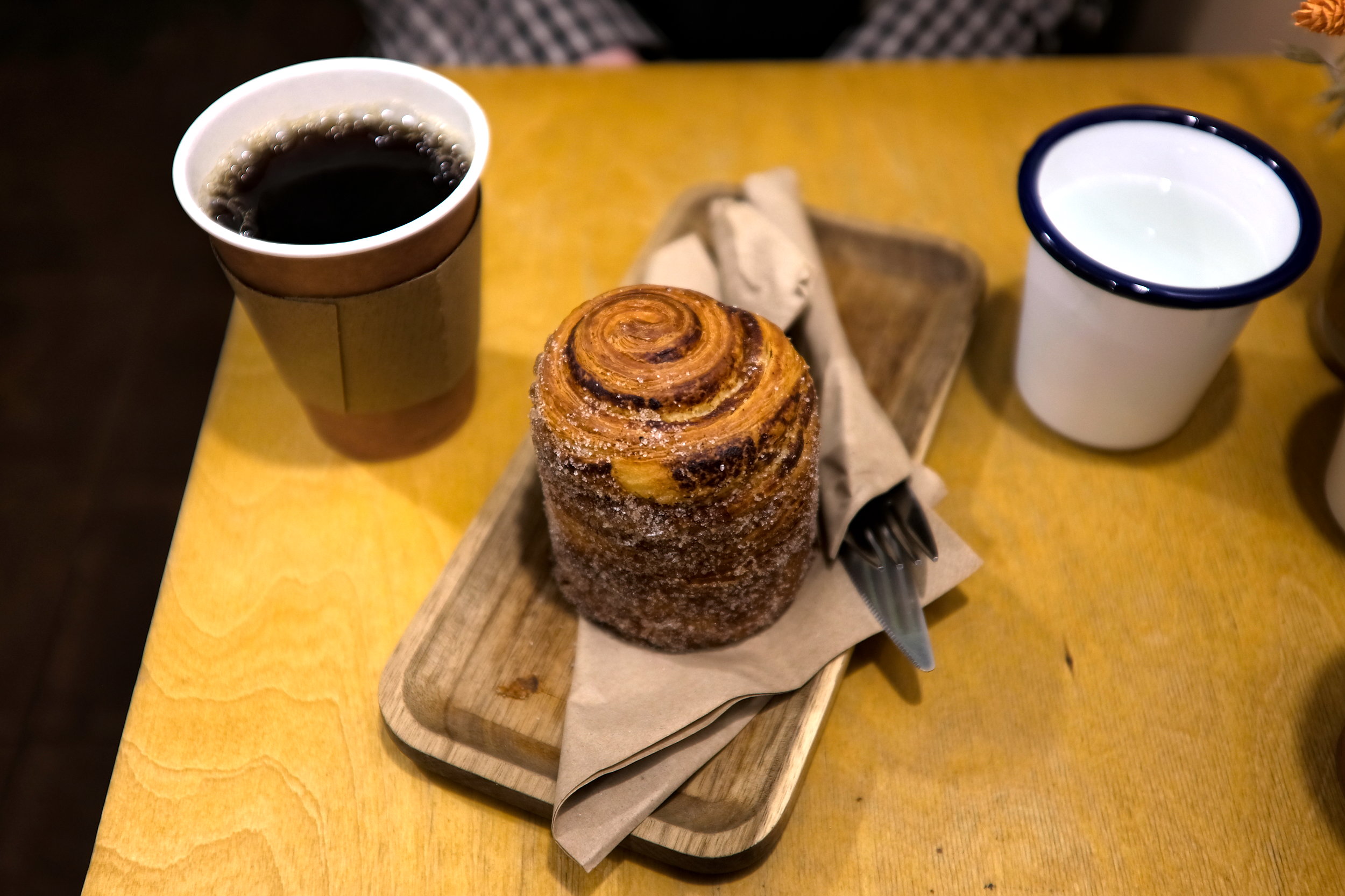 A cinnamon roll made of croissant dough on a wooden platter, with a cup of long black coffee at One Kinda Folk in Dublin