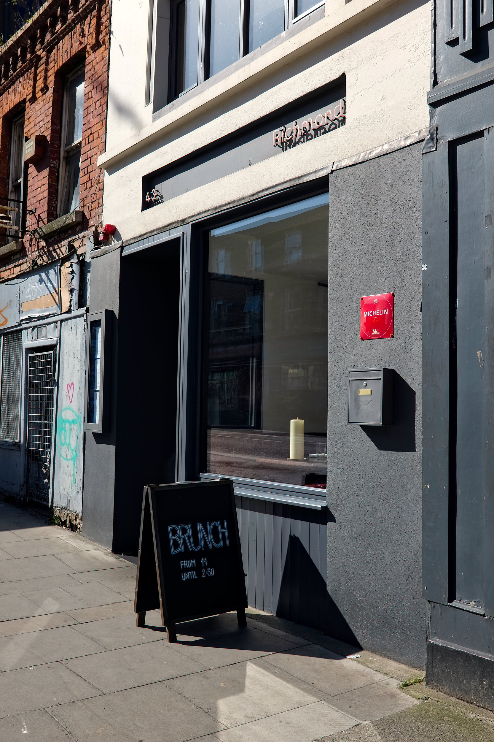 The entrance to Richmond restaurant in Dublin. The building has a grey face, with a sign that reads Richmond above in a plain font. There is a sandwich board out front advertising brunch
