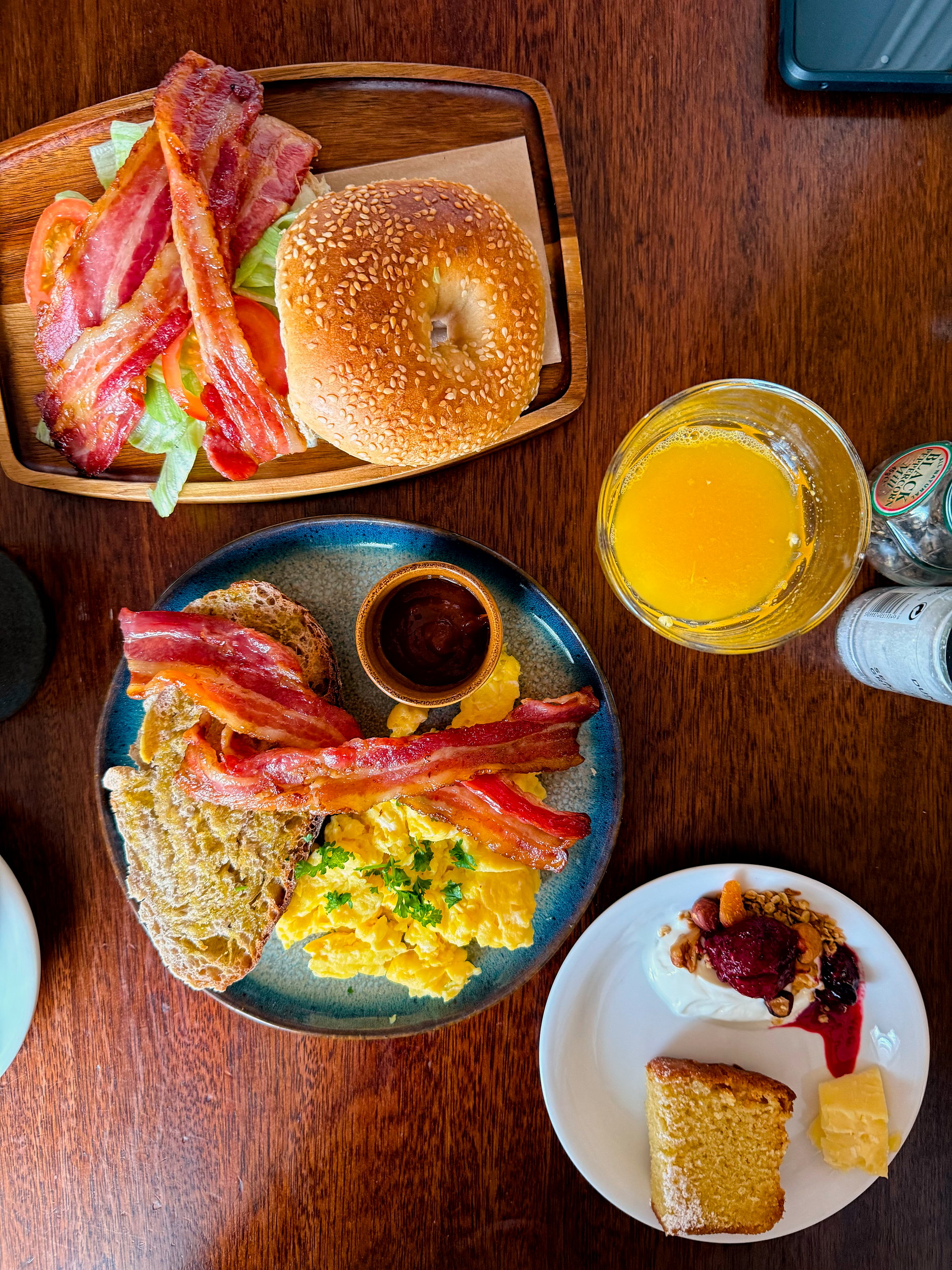 A bagel BLT and a plate of scrambled eggs, bacon, and toast from The Stop's breakfast menu, along with homemade granola and cake