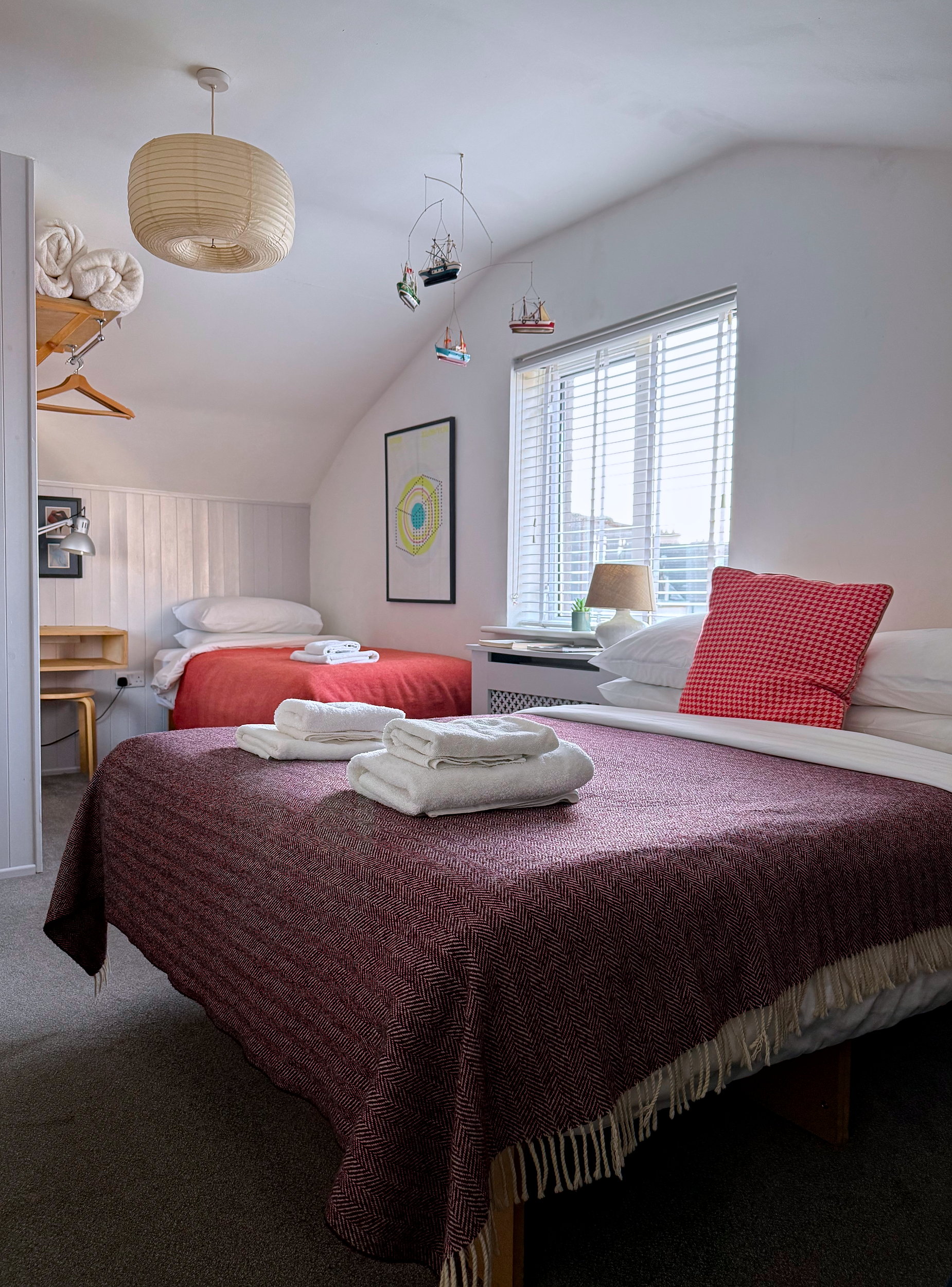 A spacious guest room at The Stop Galway with a double bed and twin bed, a small writing station with a chair, and an open wardrobe for hanging clothes.