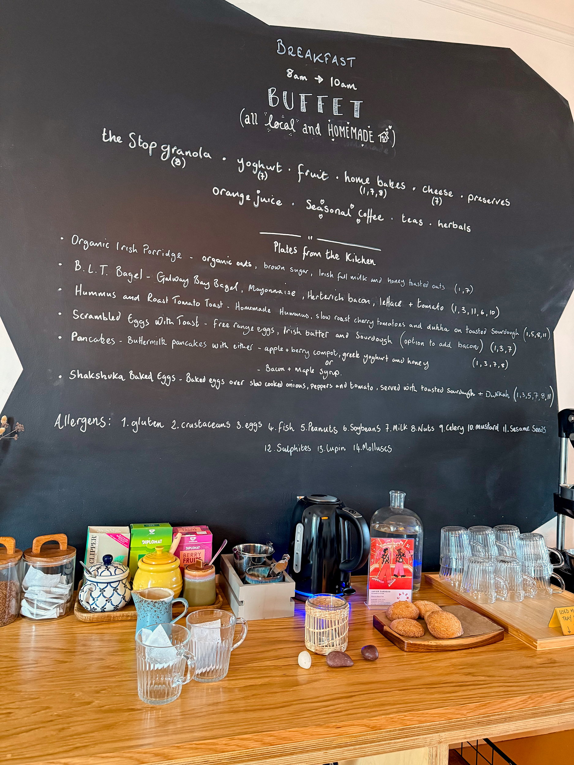 Two cups of tea waiting for the kettle to finish boiling, a plate of cookies, and a big chalkboard menu with all of the breakfast options available at The Stop