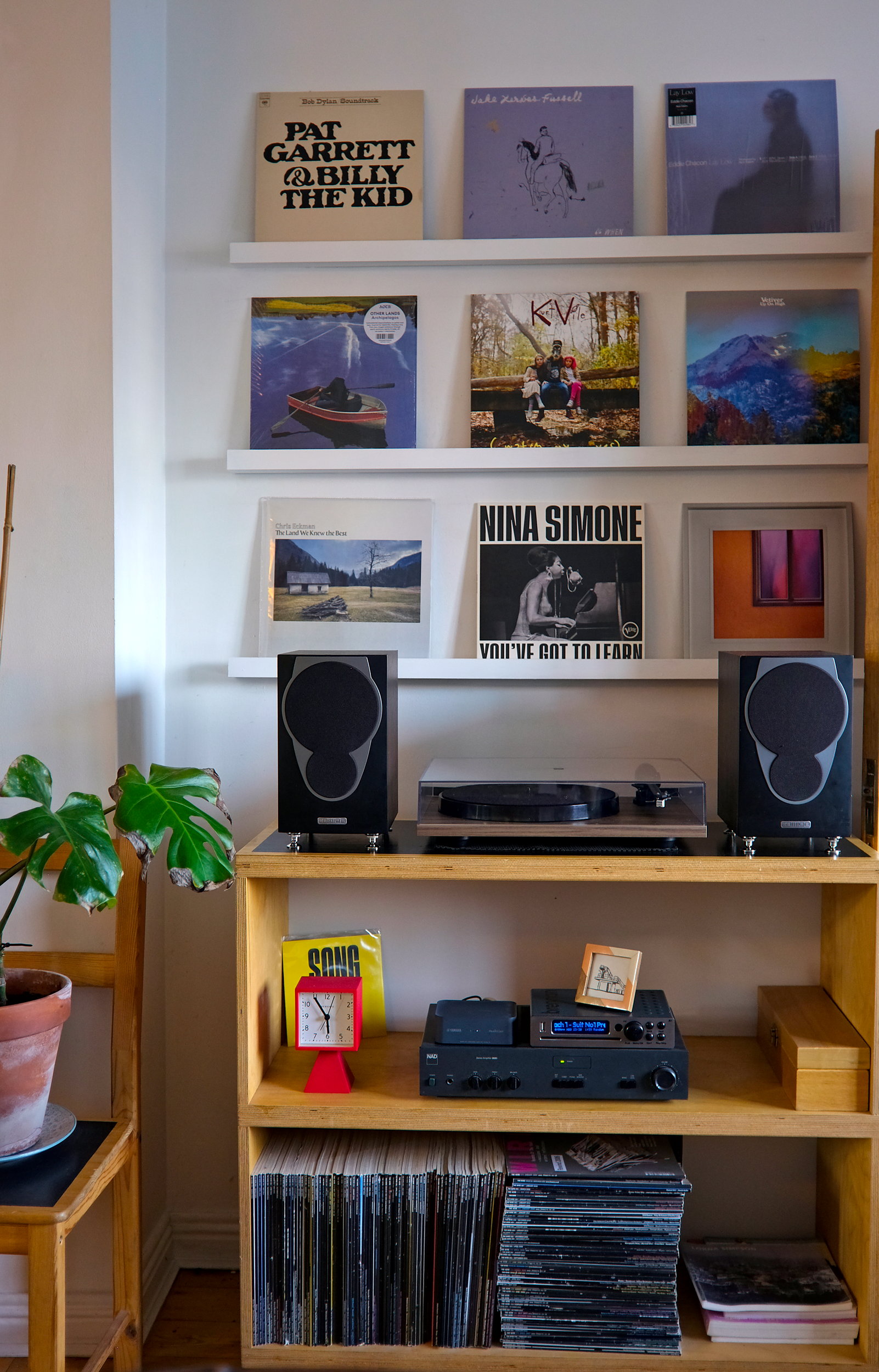 A cozy music corner inside The Stop Galway featuring a record player setup flanked by speakers, surrounded by vinyl albums including Nina Simone and Kurt Vile, with shelves holding books, a red clock, and a leafy potted plant nearby.