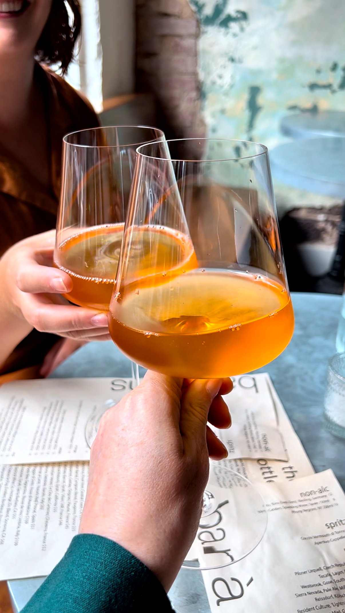 Alyssa clinks a glass of orange wine with a friend