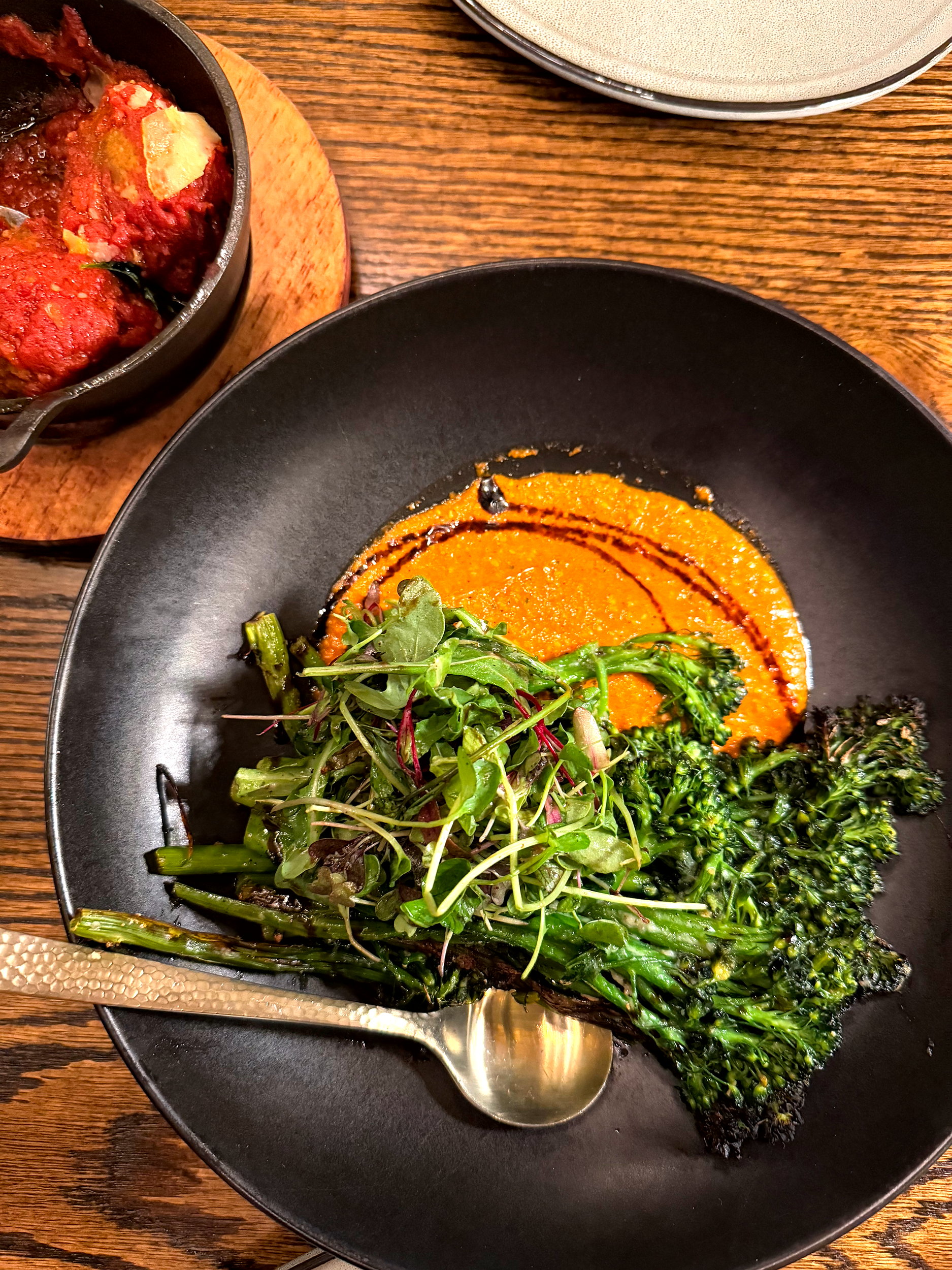 A plate of broccolini with a romesco sauce and meatballs