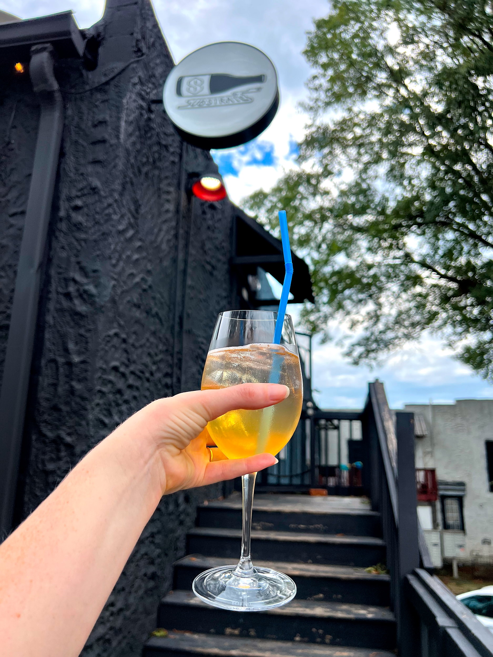 Alyssa holds a spritz up to the sign at Substrate